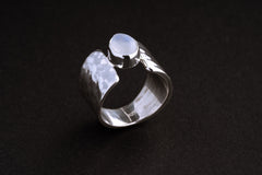 Blue Moonstone Hammered Silver Ring shown on black background with organic wide silver band and icy Moonstone centre.