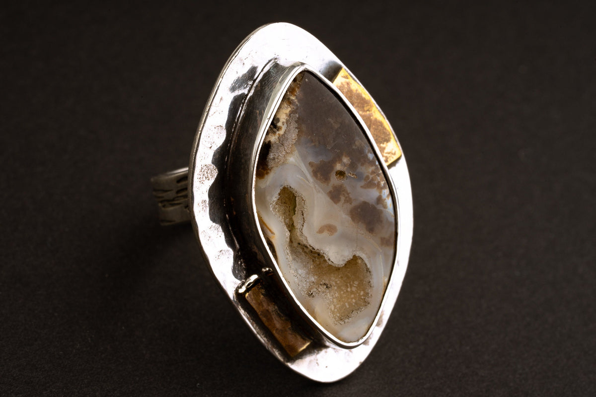Ammonite fossil adjustable ring in hammered 925 sterling silver with brass accents, shown close-up on a dark background.