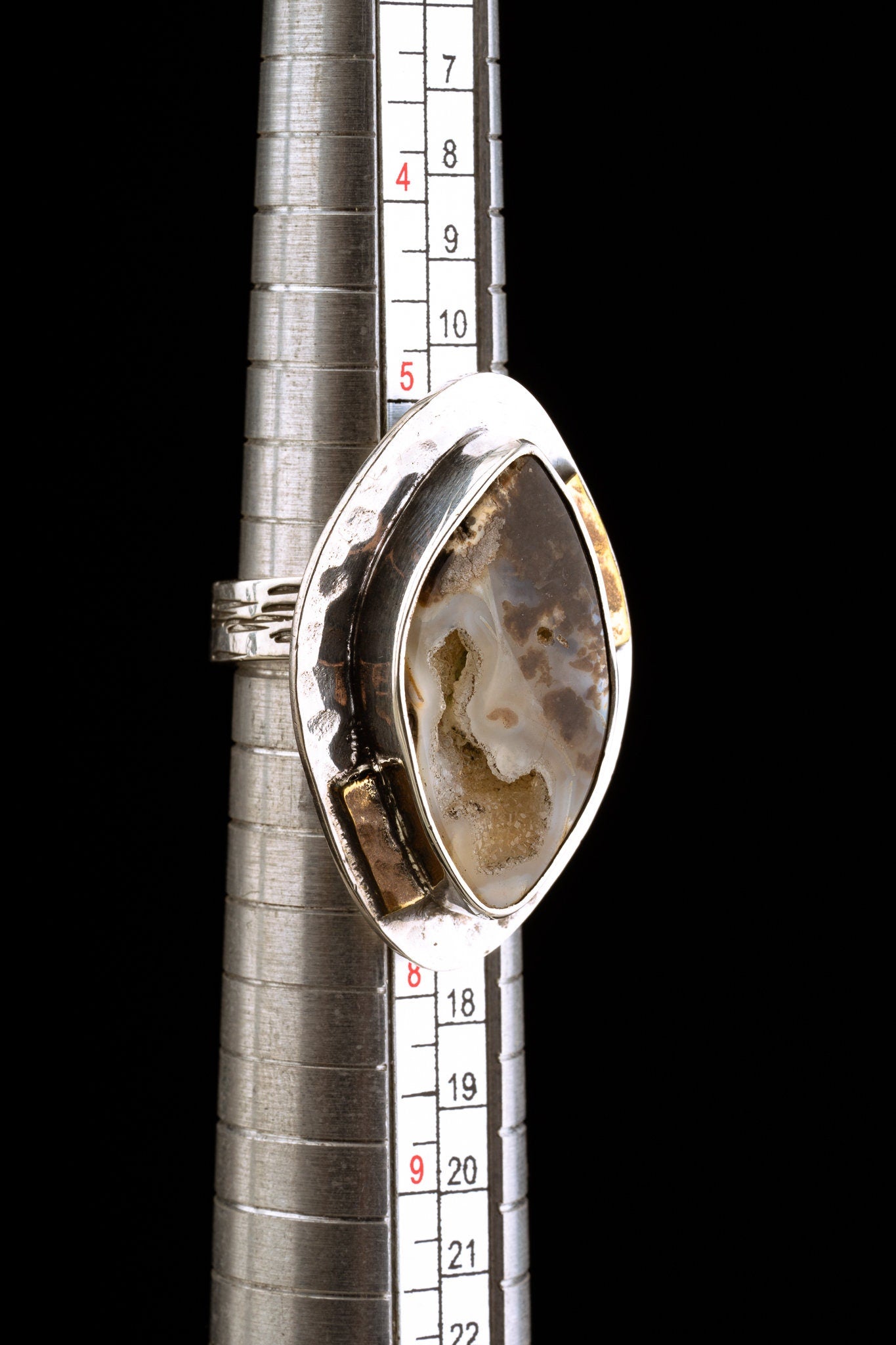 Ammonite fossil adjustable ring shown beside a ruler for scale, with mixed-metal sterling silver and brass construction.