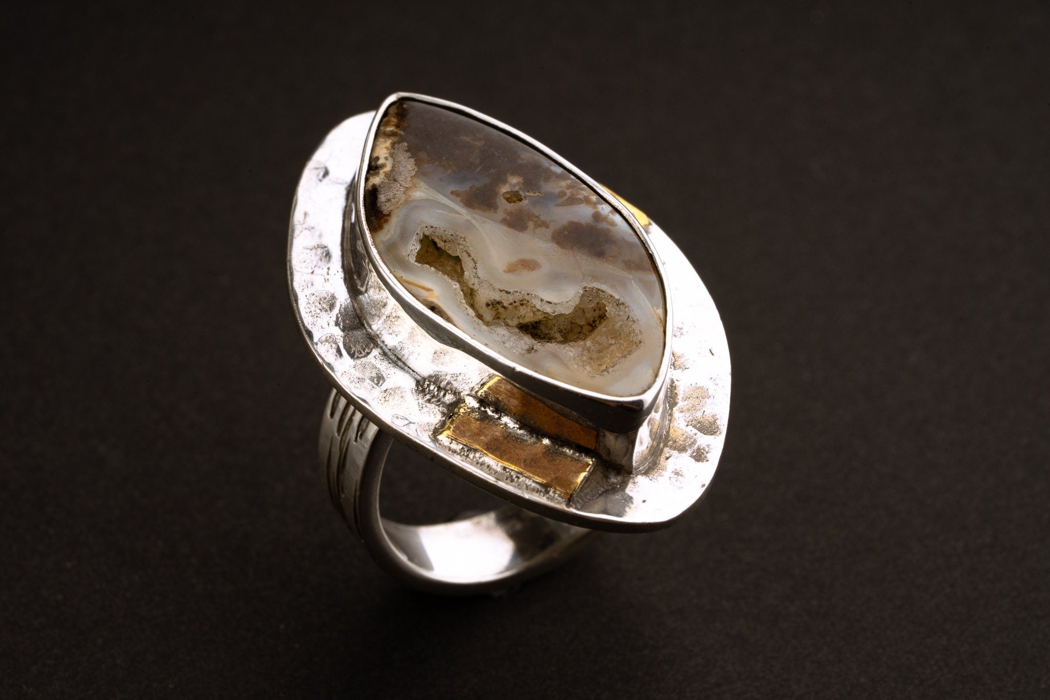 Side close-up of Ammonite fossil ring showing the widened silver bezel base, hammered texture, and brass accents.