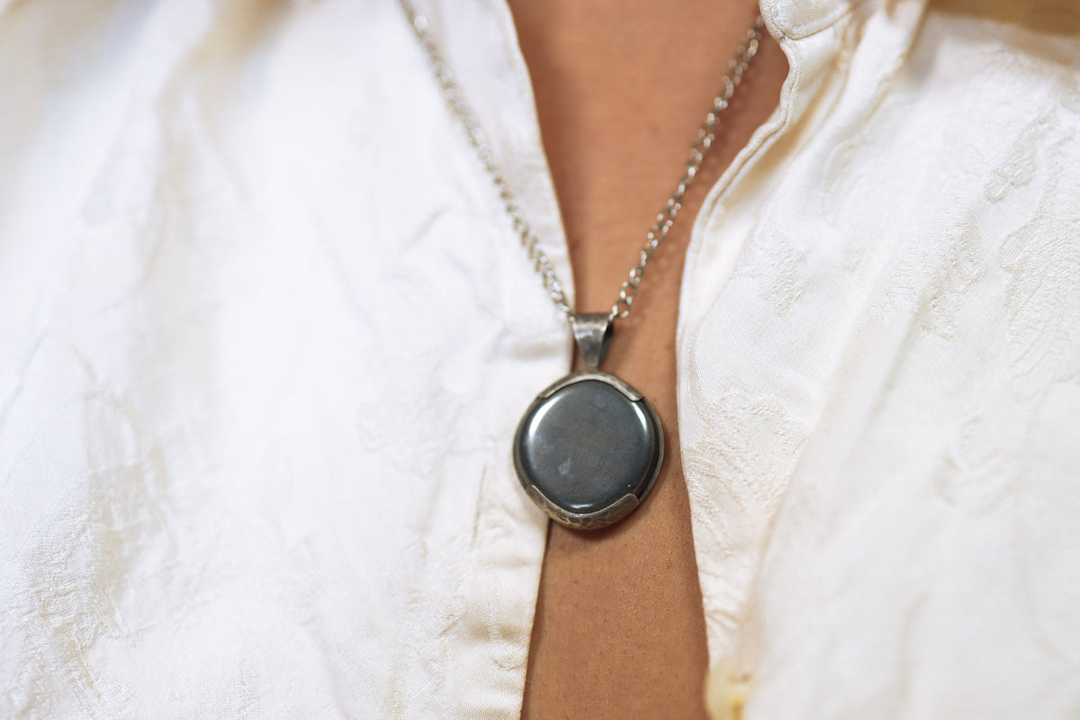 Pyrite oxidized sterling silver pendant shown on white background with open-back hammered silver setting.