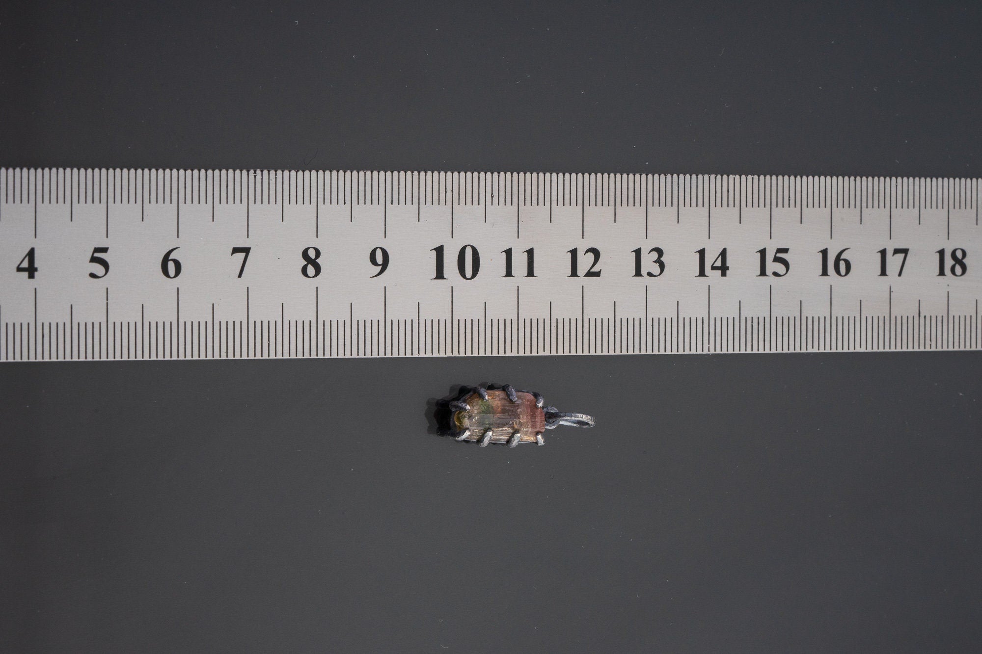 Watermelon Tourmaline pendant shown beside a ruler for scale with pink and green stone in claw setting.