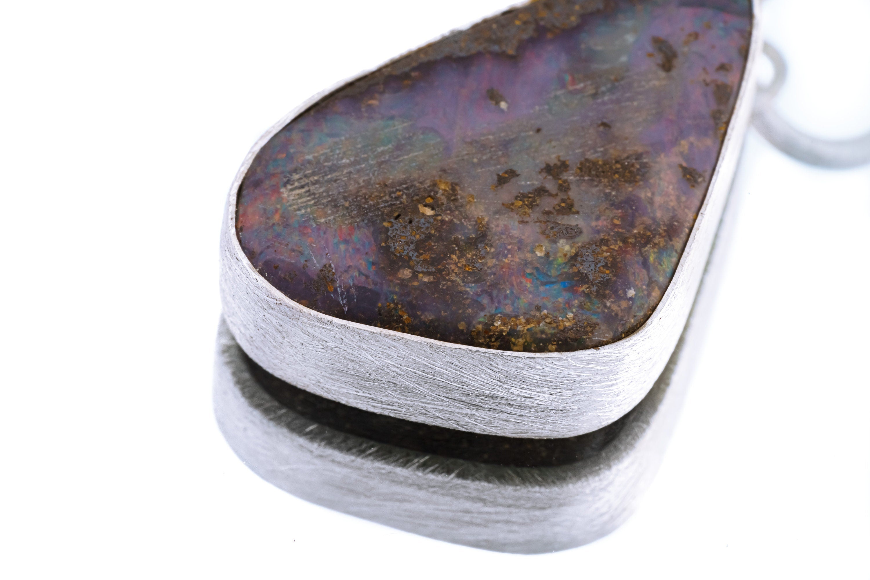 Close-up of Lightning Ridge Boulder Opal pendant showing freeform stone shape, brushed silver wall, and polished edge.
