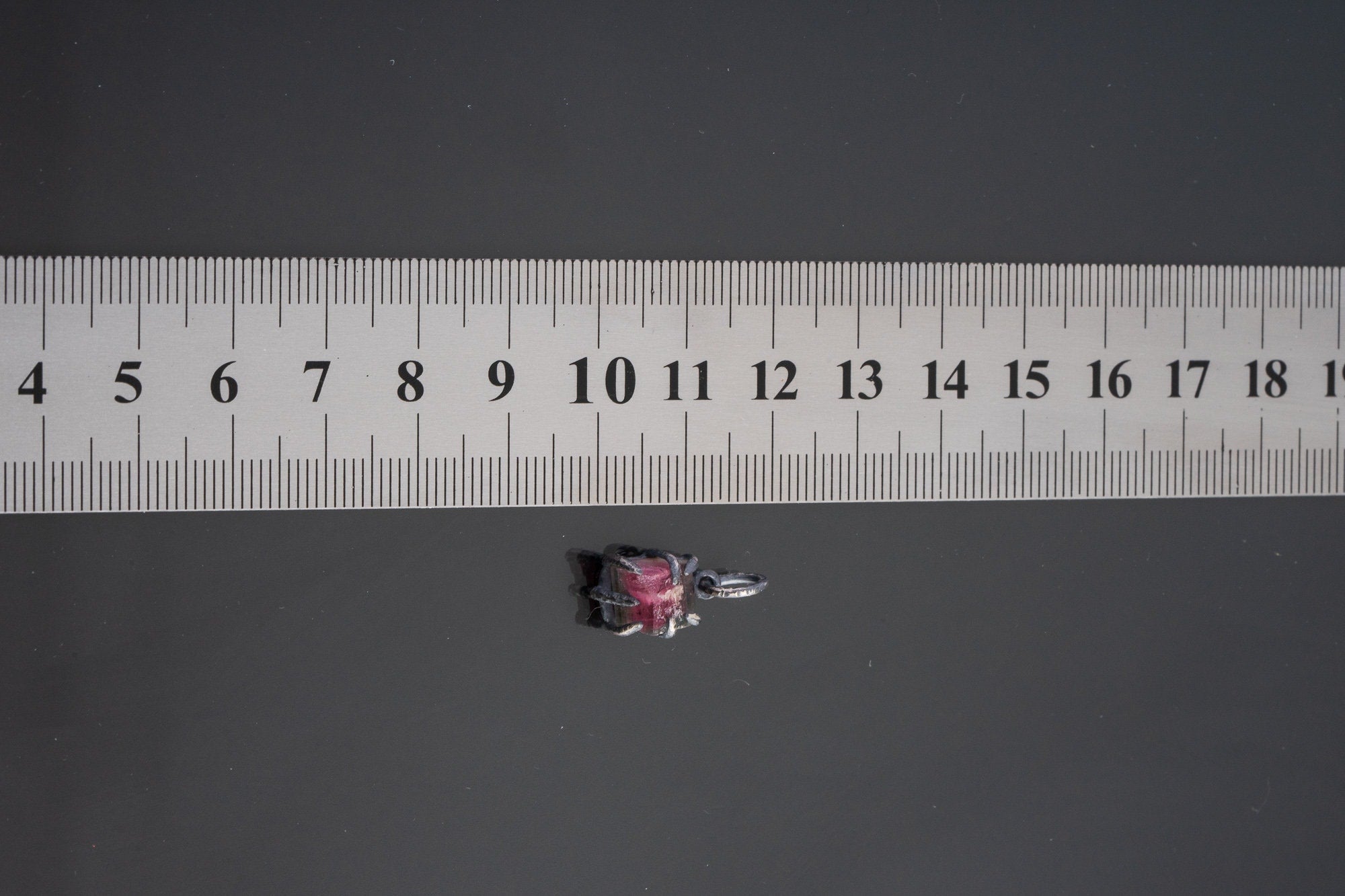 Pink Tourmaline Rubellite pendant shown beside ruler for scale 1.5cm with rose-pink crystal in oxidized silver claw setting.