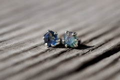 Handmade 925 sterling silver Australian Sapphire stud earrings shown on wood, with creek tumbled blue gemstones and 6-claw settings.