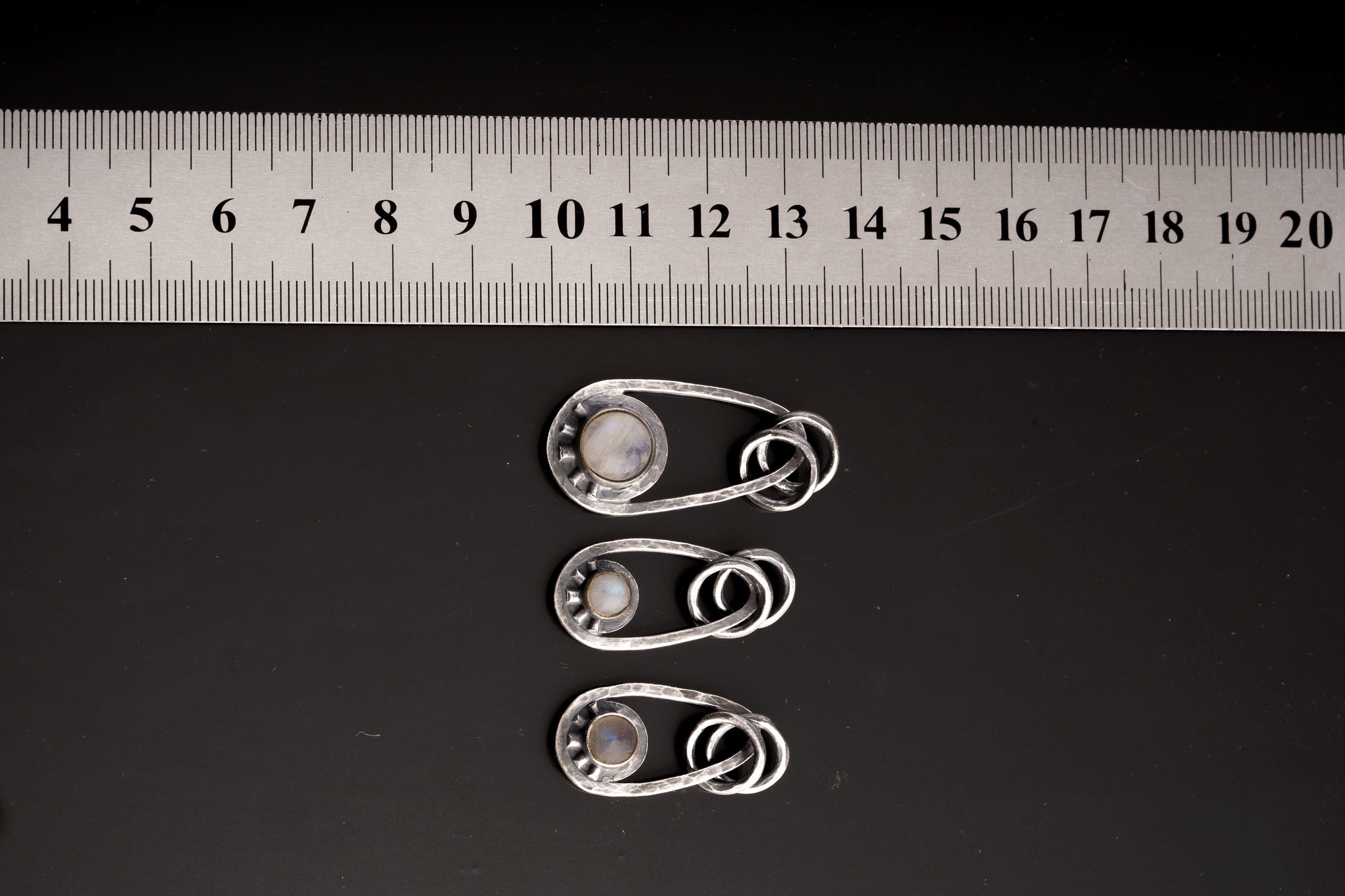 Moonstone sterling silver pendants shown beside a ruler for scale, with dual oval bails and handmade celestial ray settings.