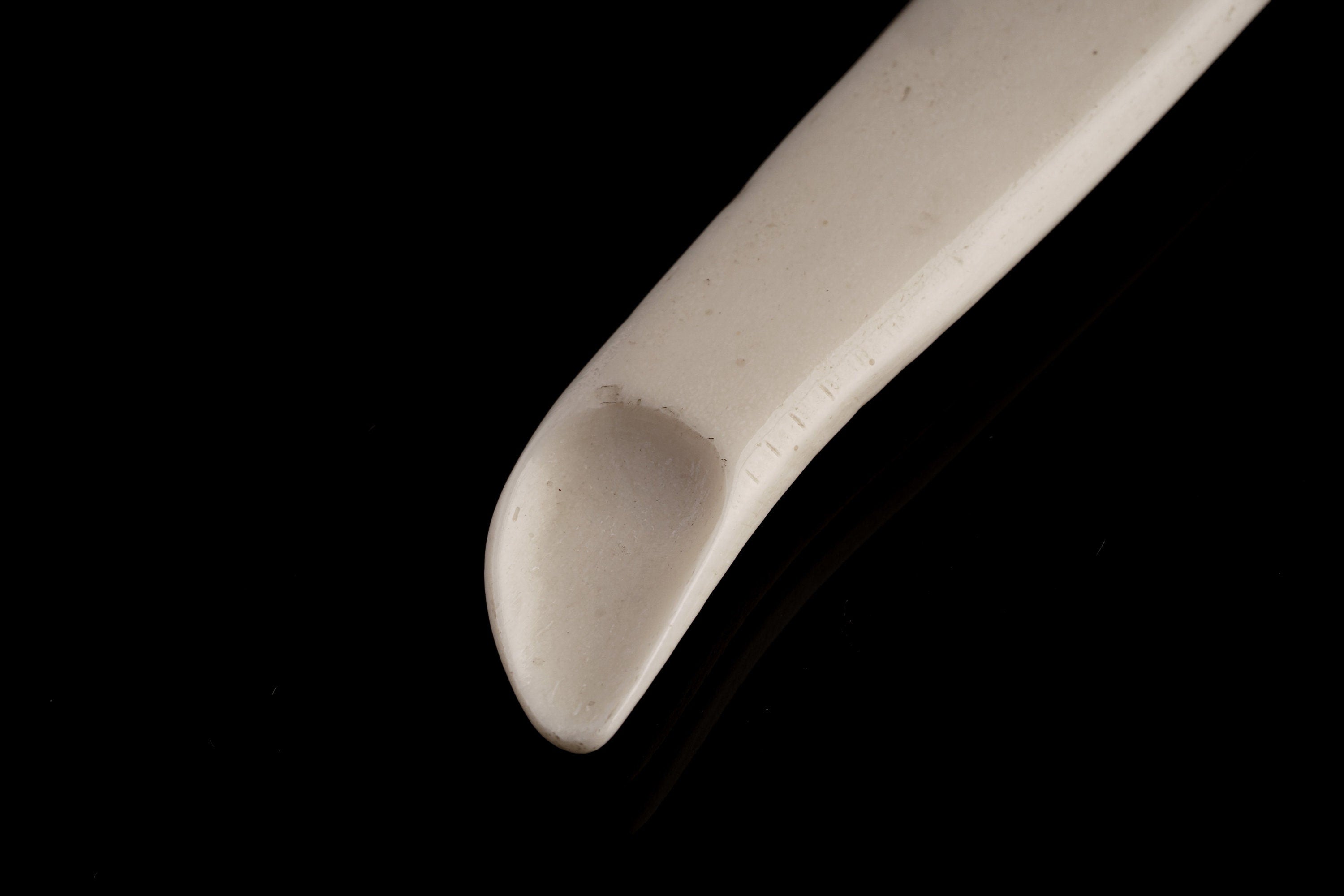 Close-up of antique bone spoon pendant tip showing carved scoop form and natural bone surface.