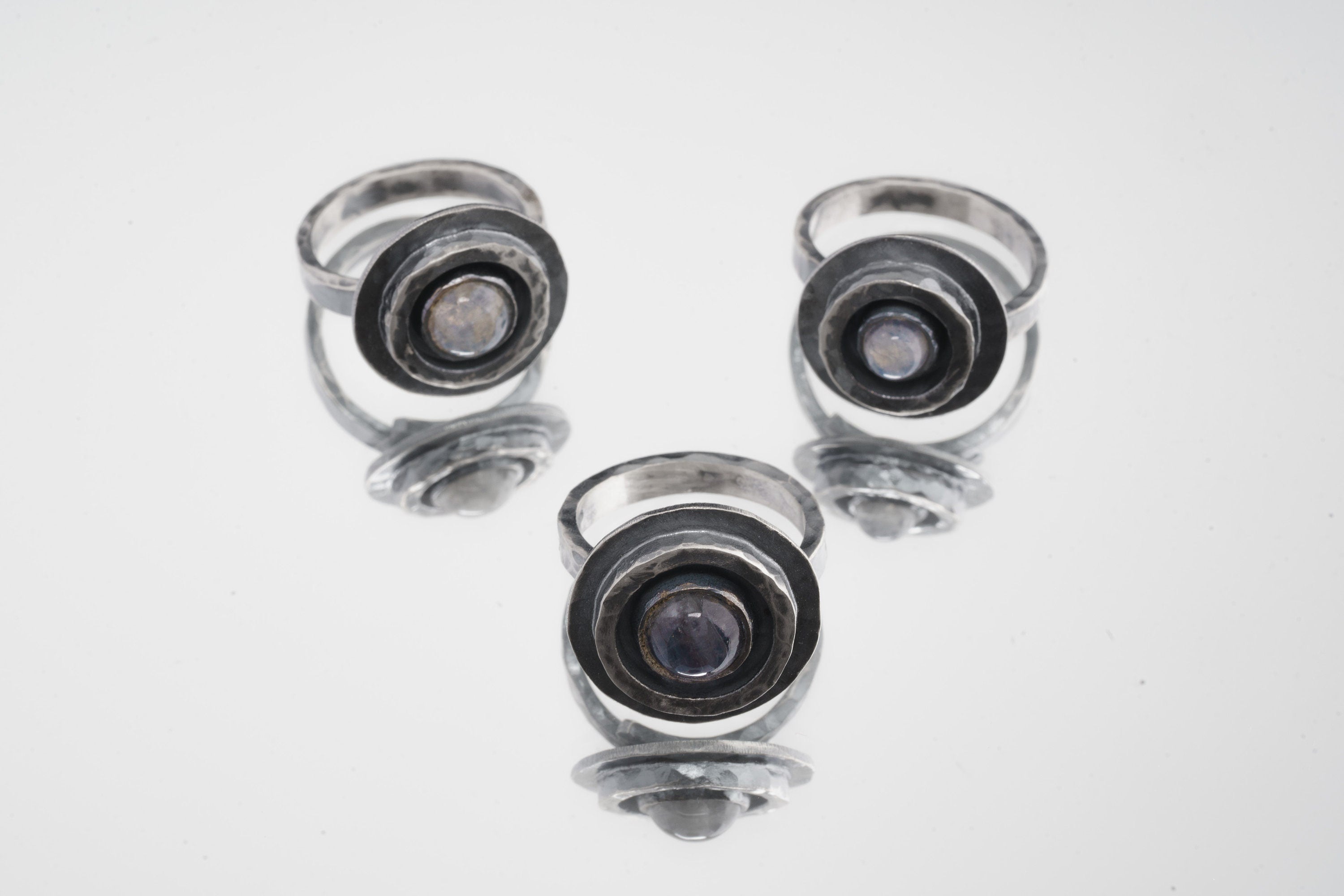 Group of Blue Moonstone Rings shown on white background with oxidized sterling silver settings and glowing cabochons.
