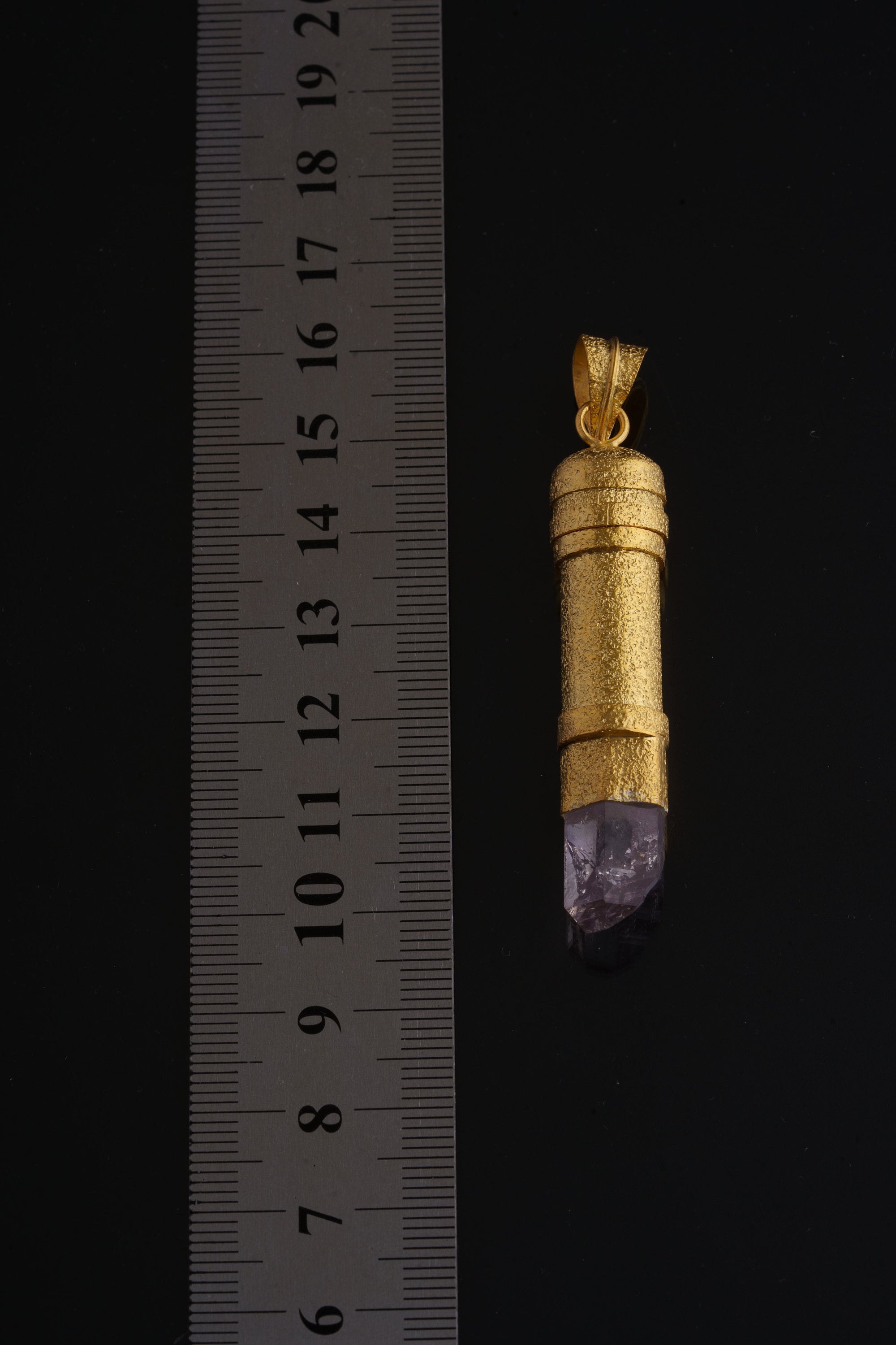 Golden capsule pendant shown beside a ruler for scale with approximately 5 cm pendant length.
