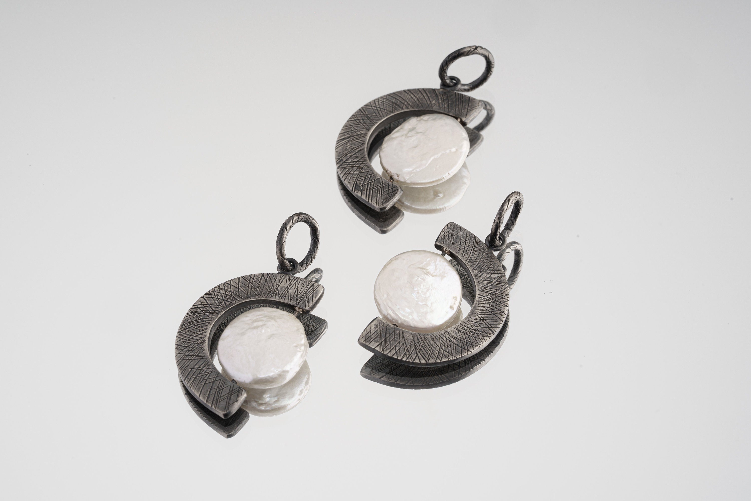 Three oxidized sterling silver Pearl crescent pendants showing natural Pearl variation and rugged crisscross texture.