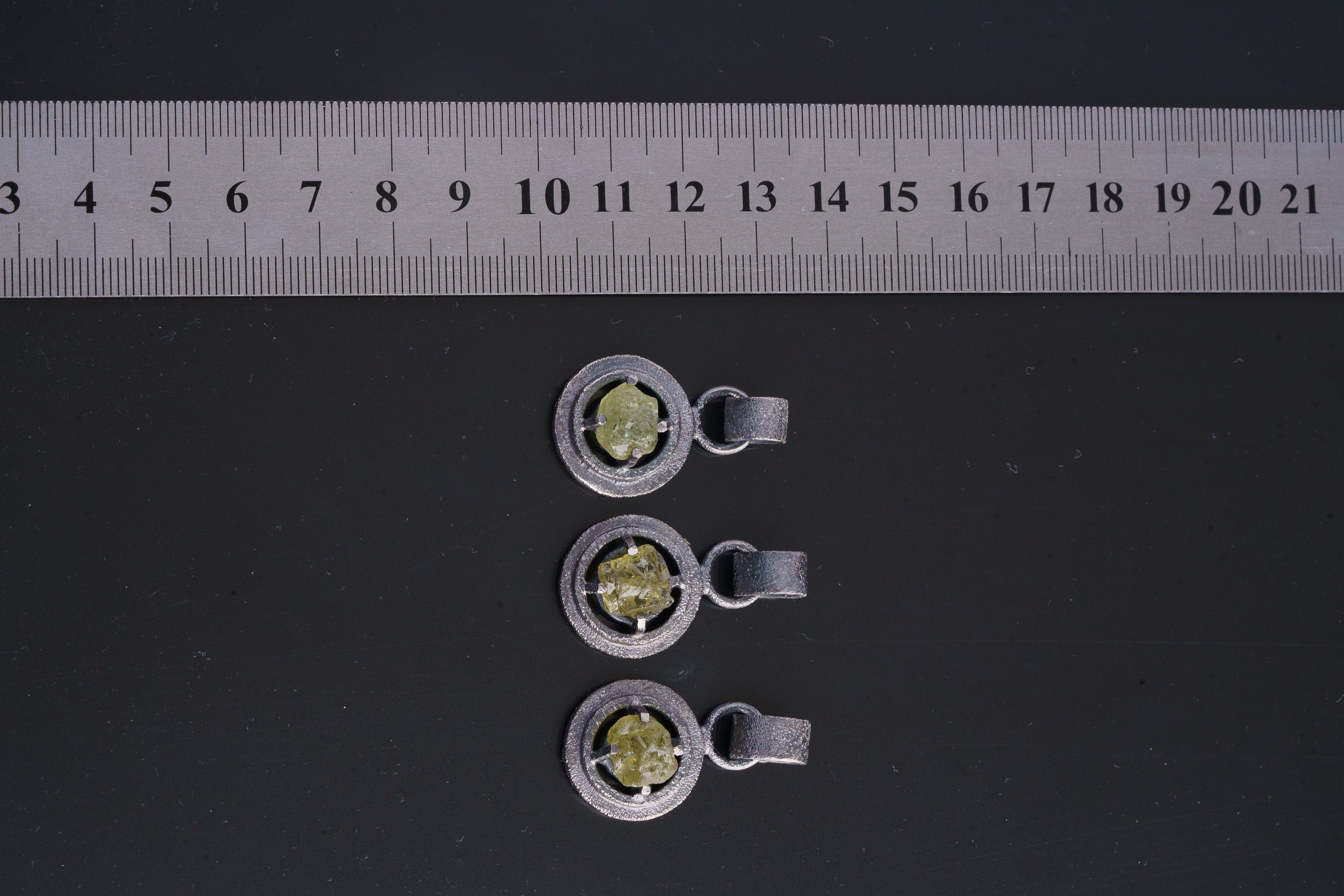 Three oxidized sterling silver Peridot claw pendants displayed on a black cord, showing handmade texture and green stones.