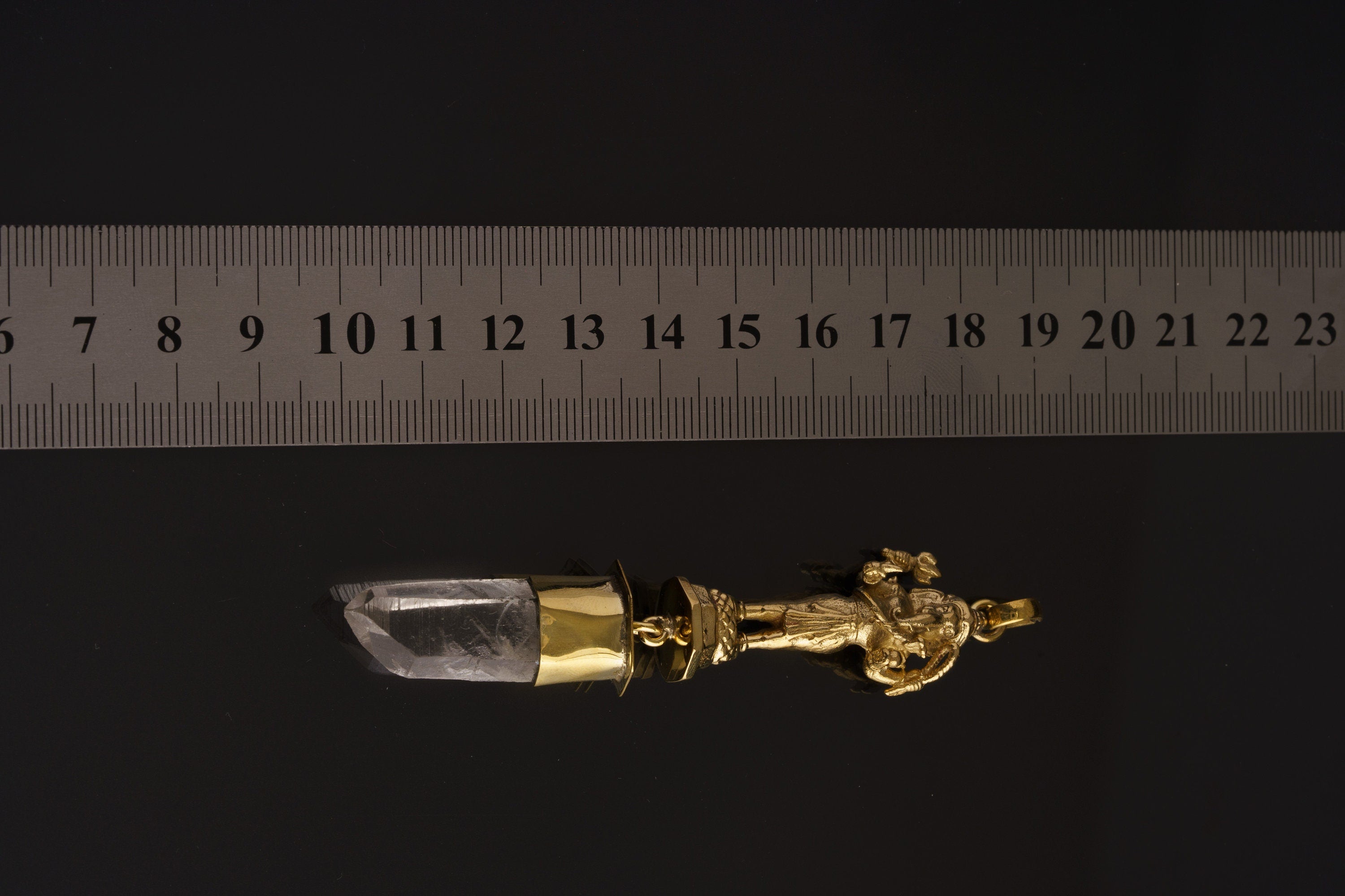 Standing Ganesha Clear Quartz pendant shown beside a ruler for scale with brass figure and crystal point.