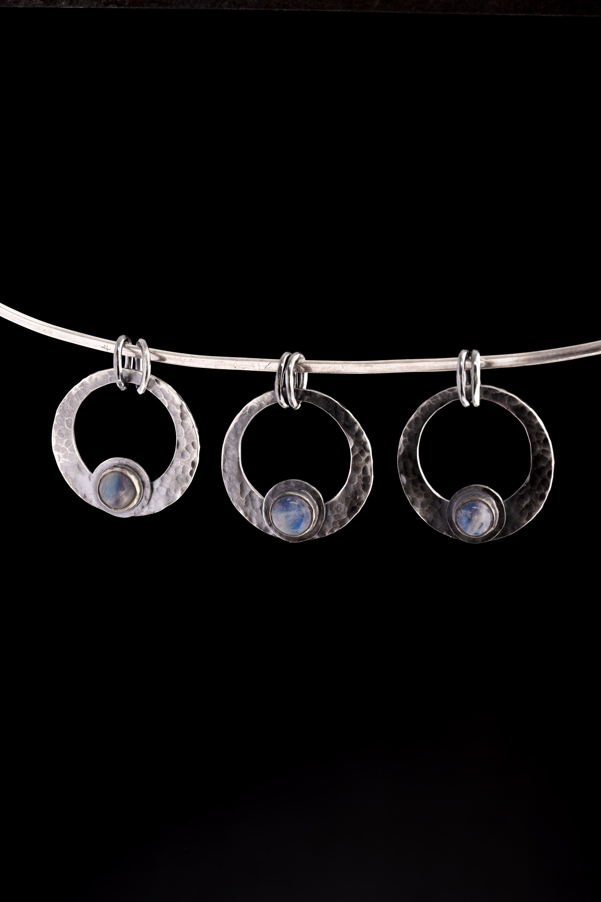 Three Blue Moonstone crescent pendants in oxidized sterling silver, showing natural stone variation and hammered texture.