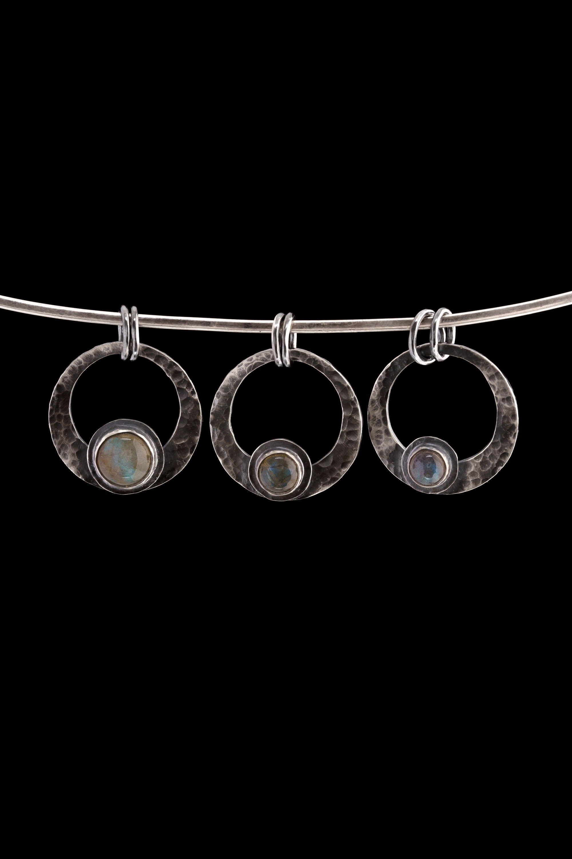 Three oxidized sterling silver crescent moon pendants with Rainbow Labradorite stones hanging on a black cord.
