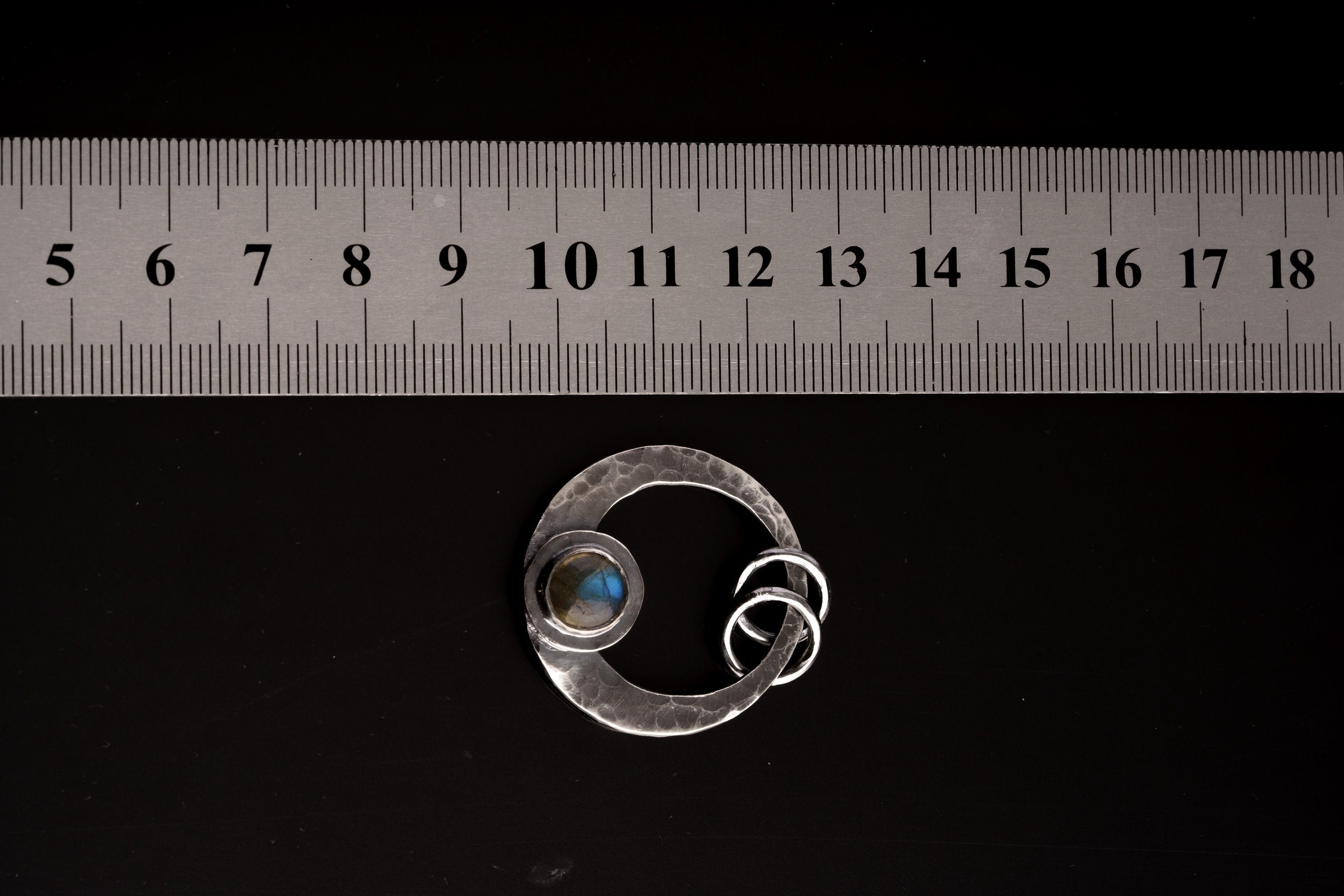 Rainbow Labradorite crescent moon pendant shown beside a ruler for scale, with hammered oxidized silver and dual oval bail.