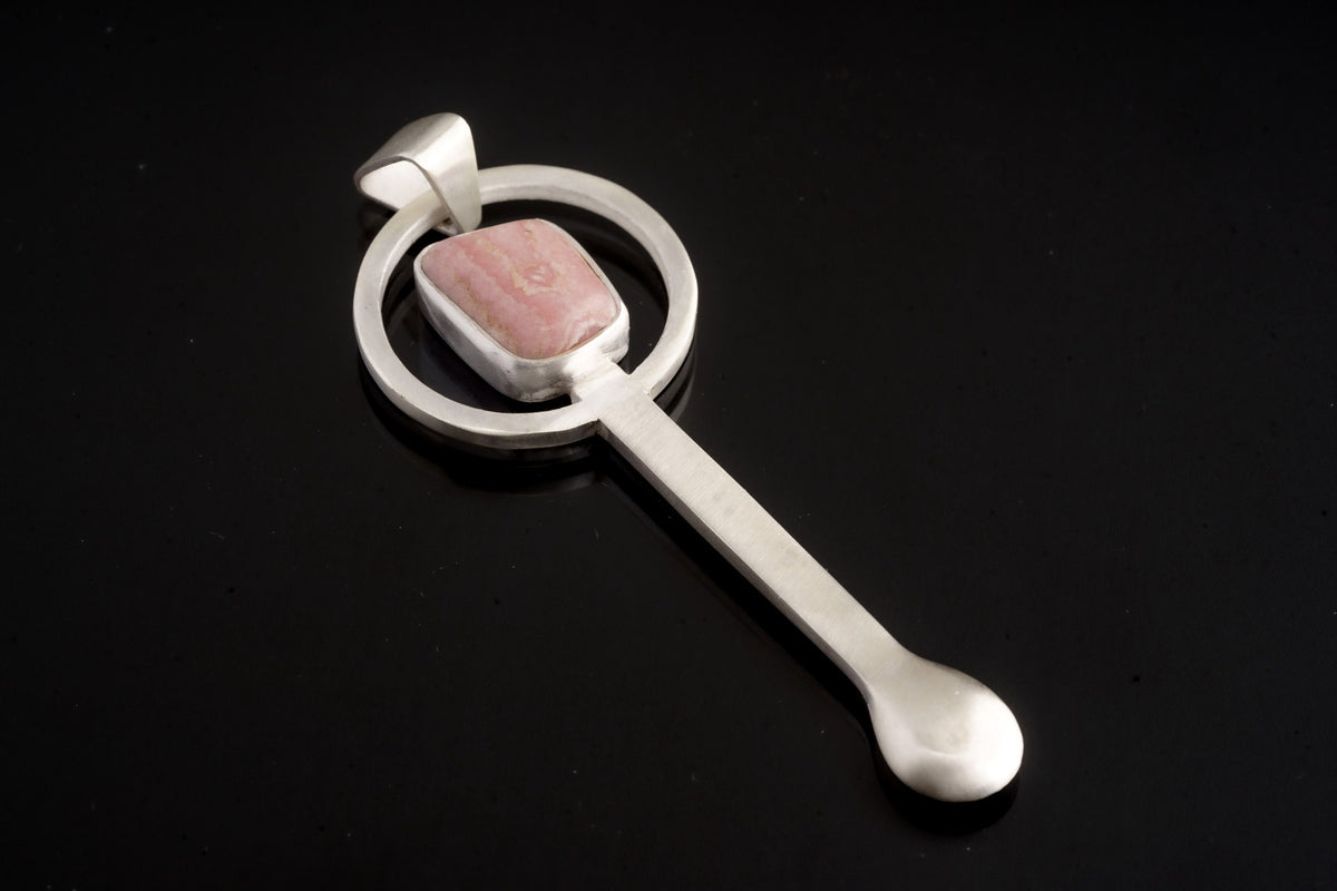 Rhodochrosite sterling silver hammered spoon pendant shown on dark background with pink stone and sculptural spoon form.