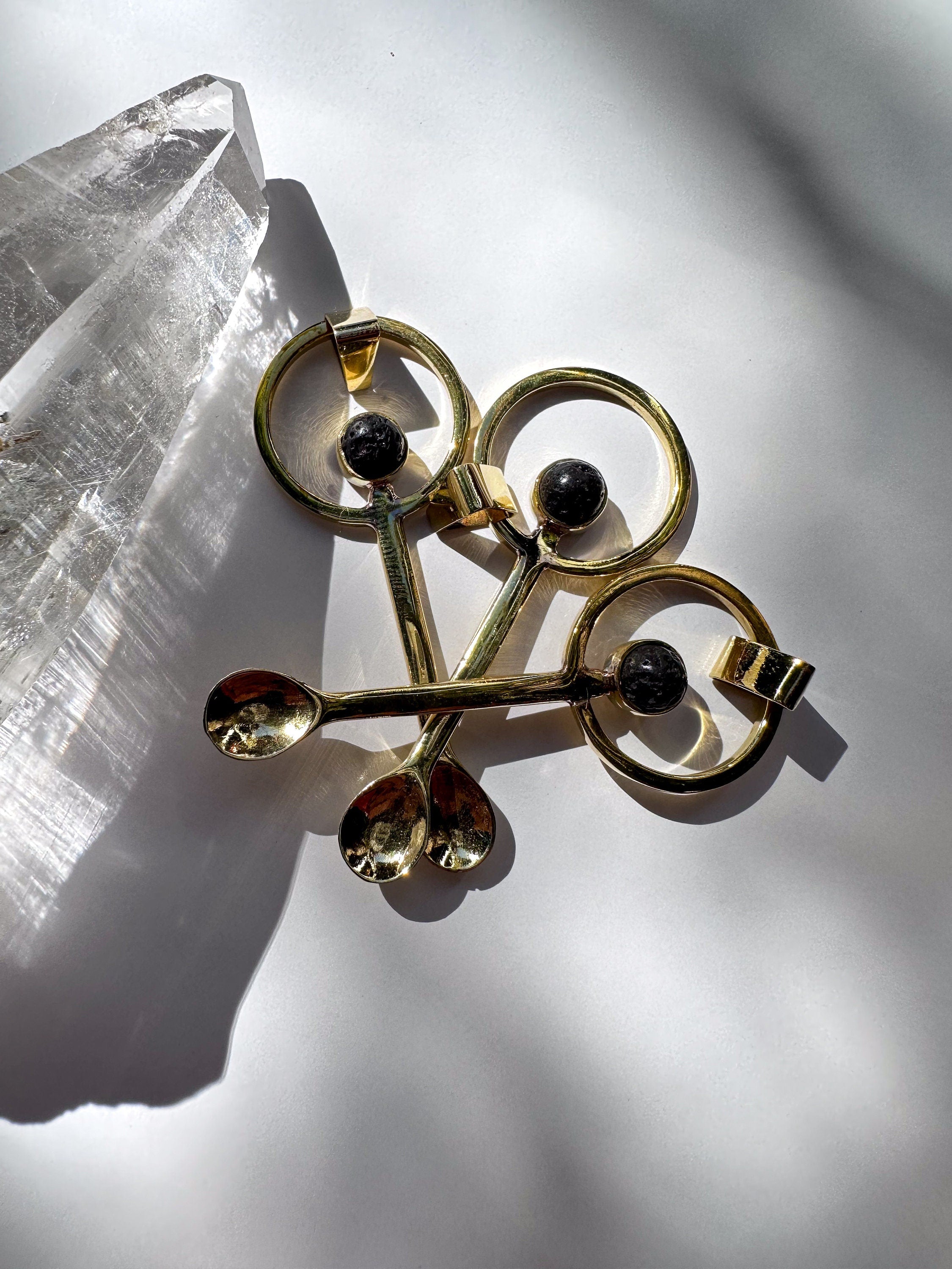 Collection of gold-plated brass ritual spoons with volcanic stone and gemstone cabochons shown in sunlight.