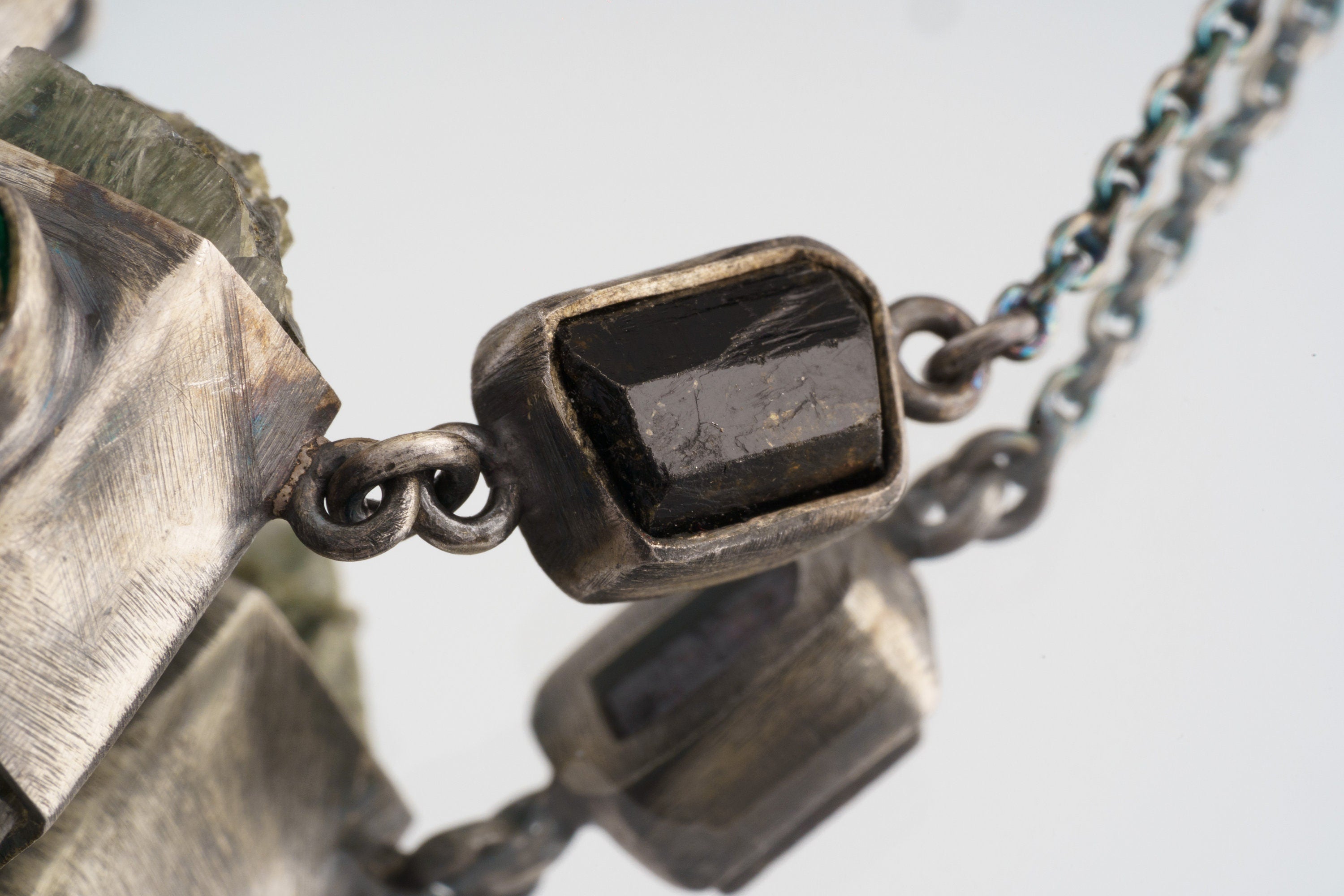 Close-up of dark faceted Garnet accent beside the sterling silver chain on the Verdant Quartz Relic Necklace.
