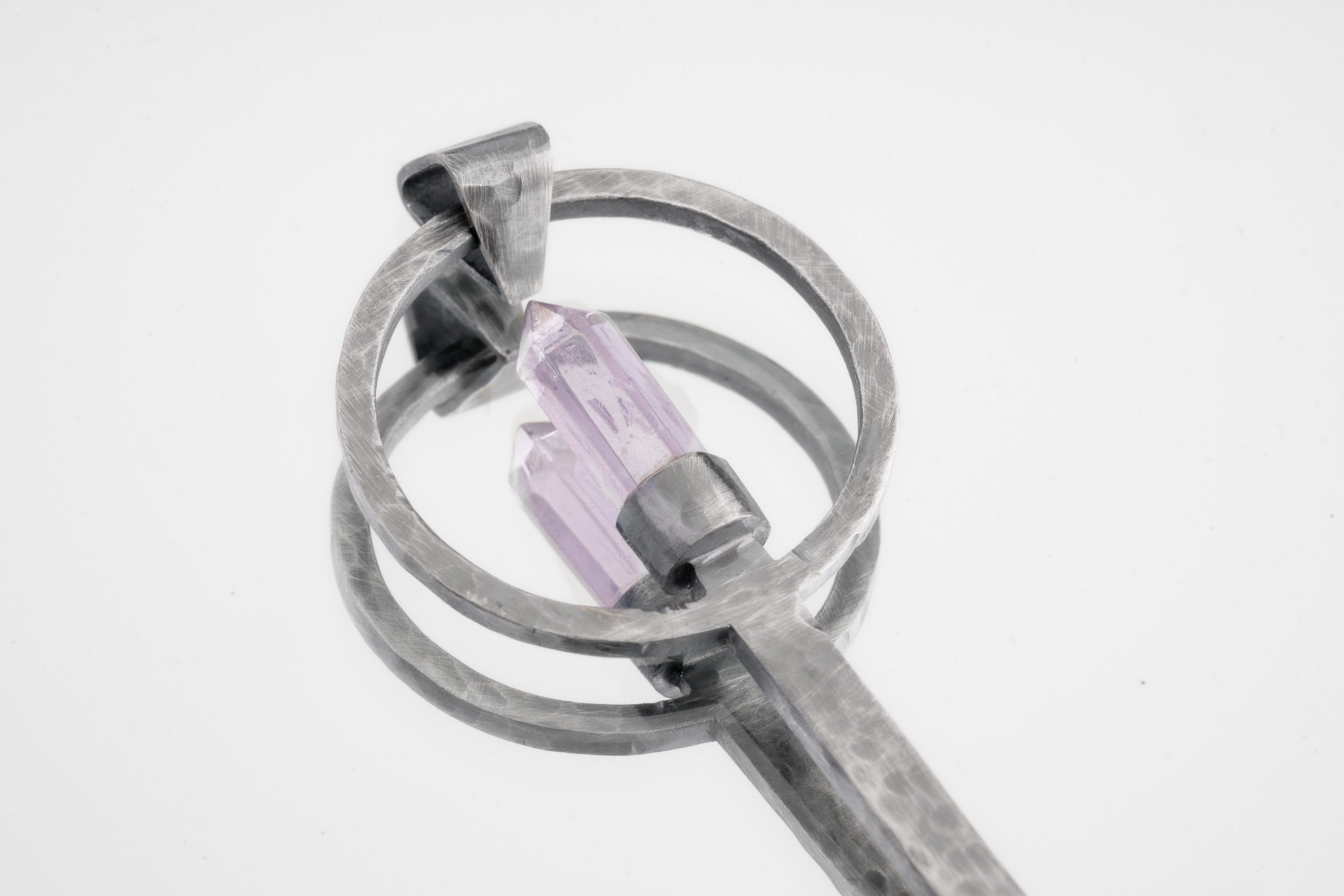 Close-up of Amethyst Generator spoon showing brushed sterling silver texture and pointed purple crystal setting.