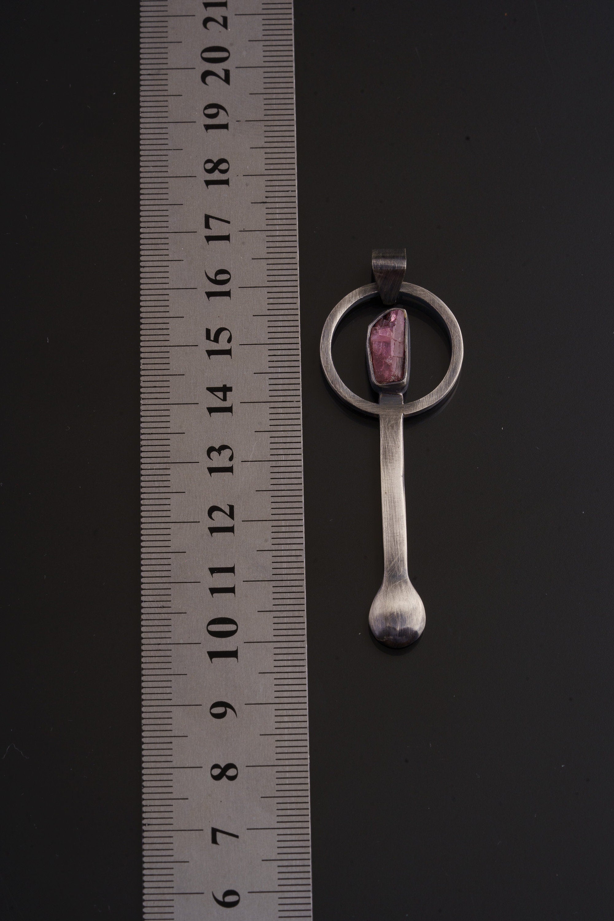 Rubellite Tourmaline sterling silver spoon pendant shown beside a ruler for scale with brushed silver body and pink-red stone.