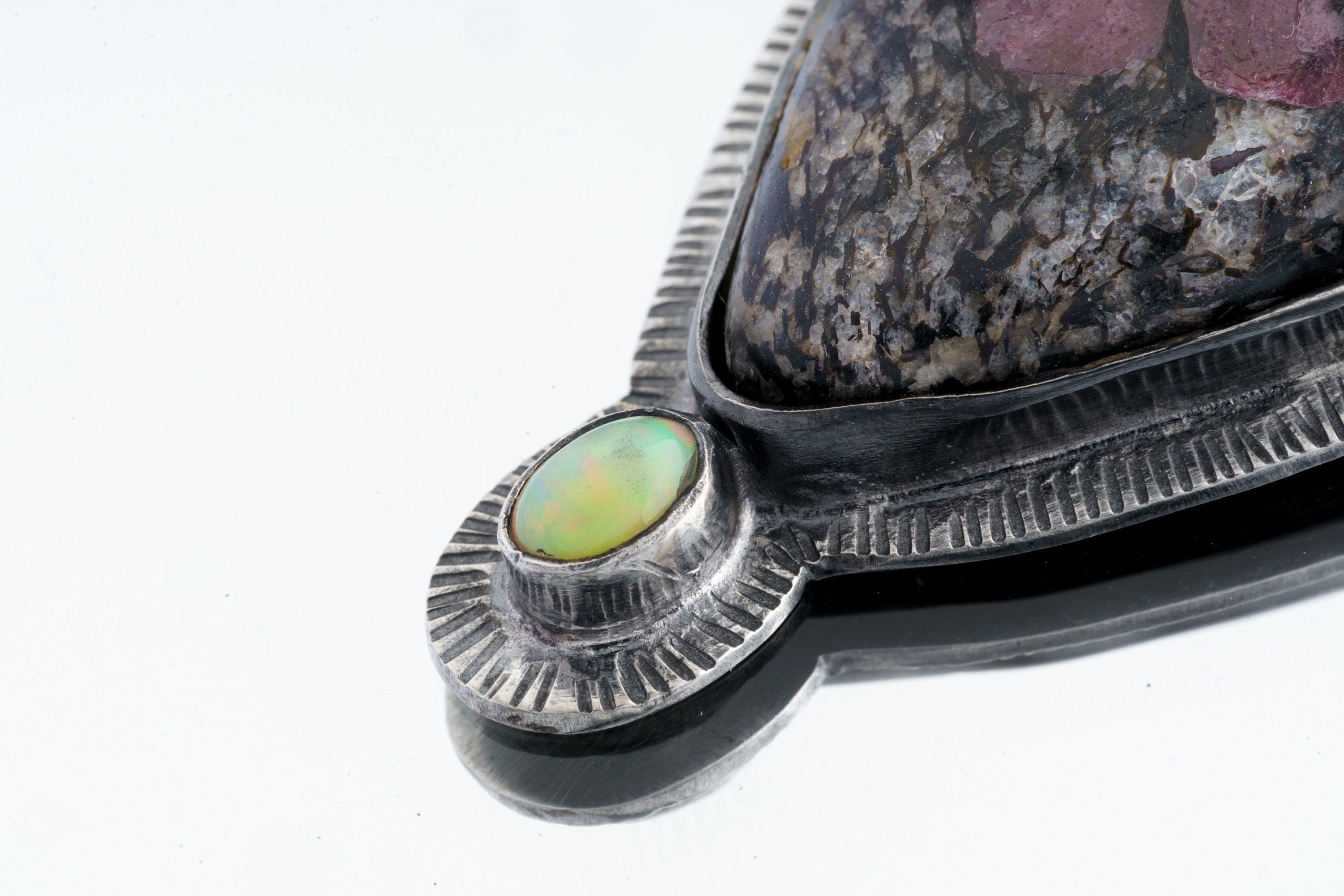 Close-up of Ruby in Black Matrix Ethiopian Opal pendant showing opal accent and textured sterling silver sun-ray detail.