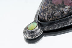 Close-up of Ruby in Black Matrix Ethiopian Opal pendant showing opal accent and textured sterling silver sun-ray detail.