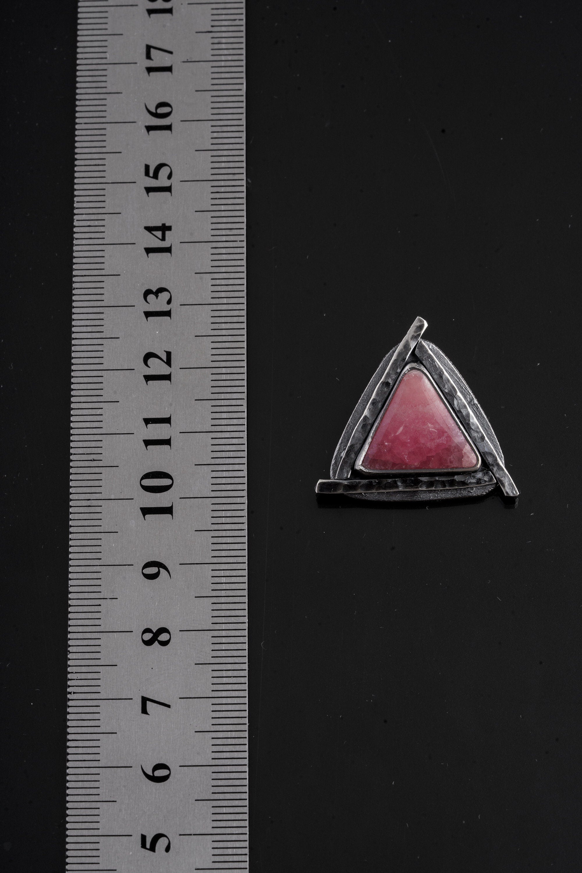 Rhodochrosite triangle pendant shown beside a ruler for scale with oxidized sterling silver frame.
