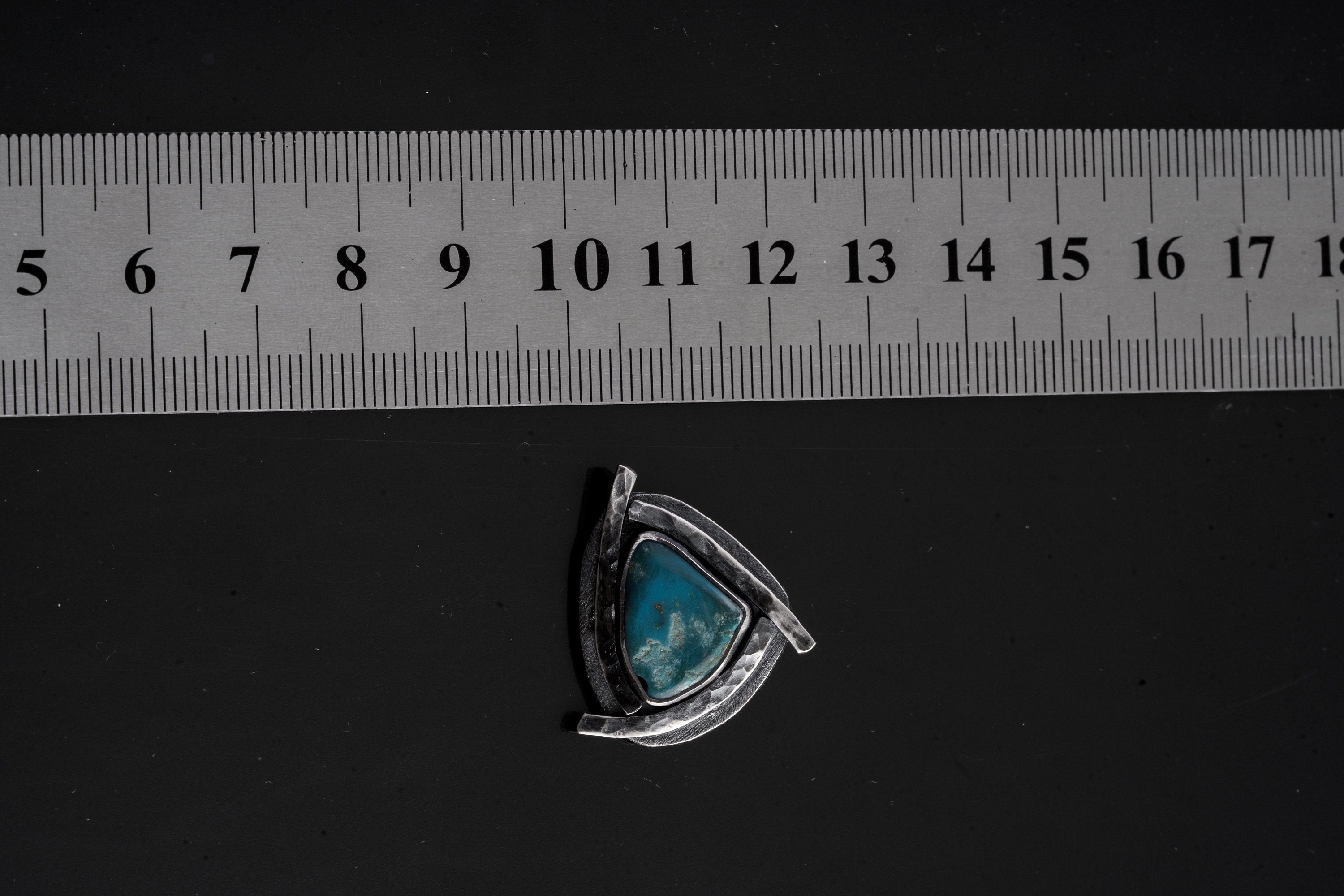Sleeping Beauty Turquoise triangle pendant shown beside a ruler for scale with oxidized sterling silver sun detailing.