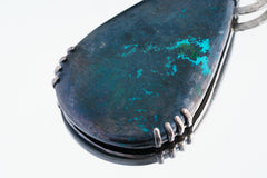Close-up of raw teardrop Moonstone in brutalist oxidized silver claw setting with blue-green mineral tones.