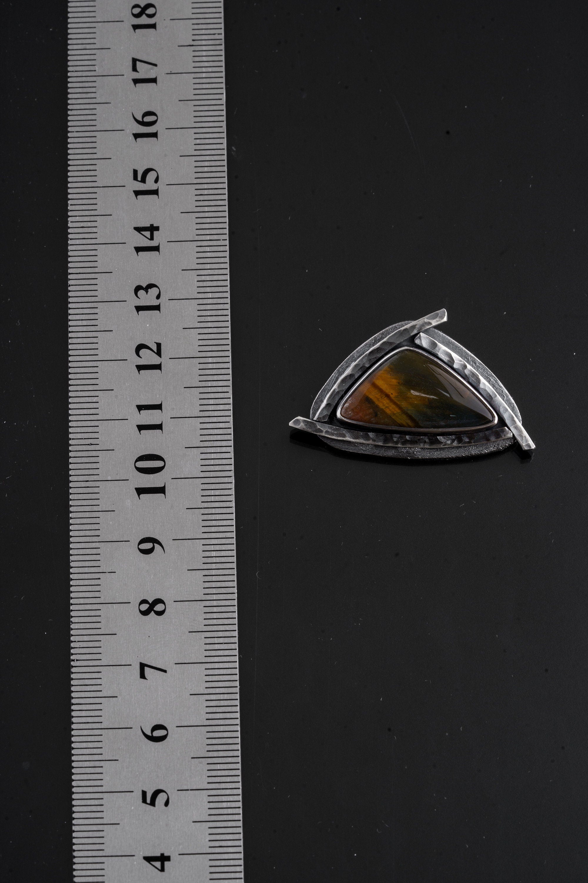 Tiger Eye triangle pendant shown beside a ruler for scale with oxidized sterling silver sun detailing.