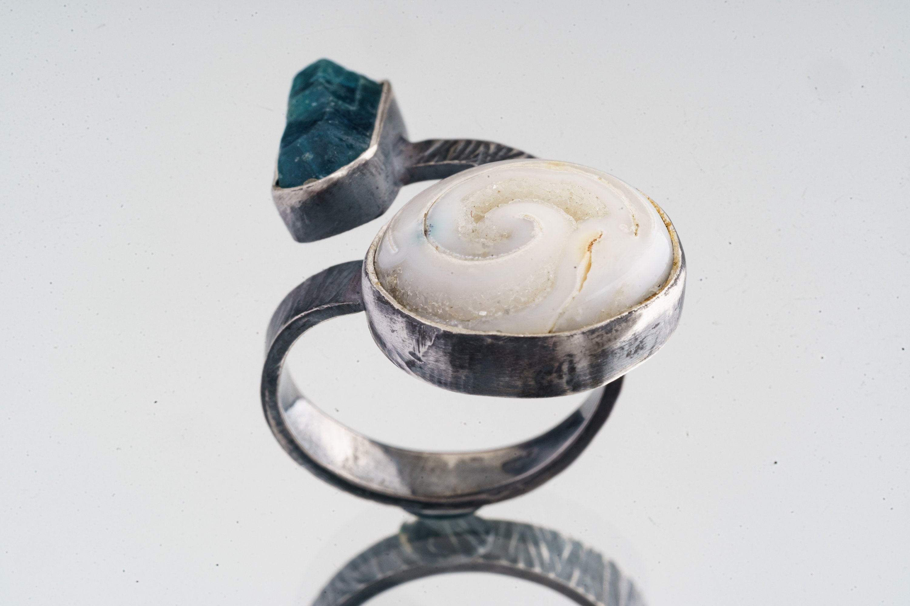 Land and Sea Apatite Shell ring shown on a white background, with blue terminated crystal and fossilized shell setting.
