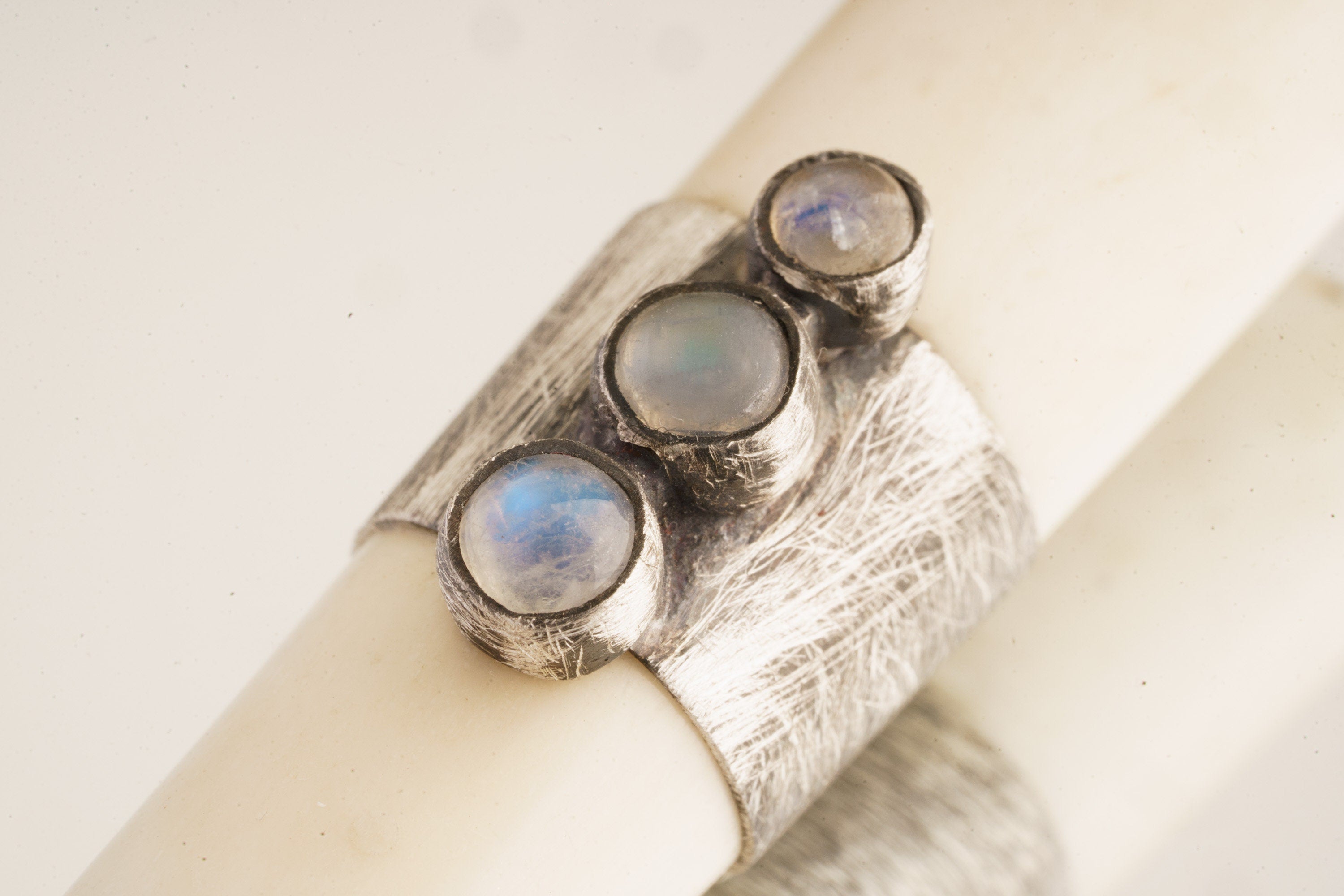 Close-up of antique bone tube pendant showing textured 925 sterling silver band and three Blue Moonstone settings.