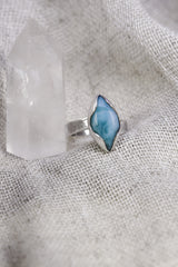 Larimar adjustable ring shown beside a quartz crystal, with high-shine sterling silver and ocean-blue eye-shaped stone.