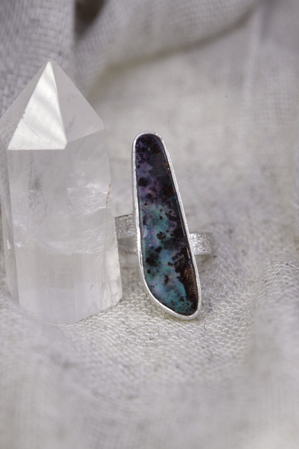 Opal sterling silver ring on soft fabric, showing the high-shine finish, textured band, and luminous blue-green colour play.