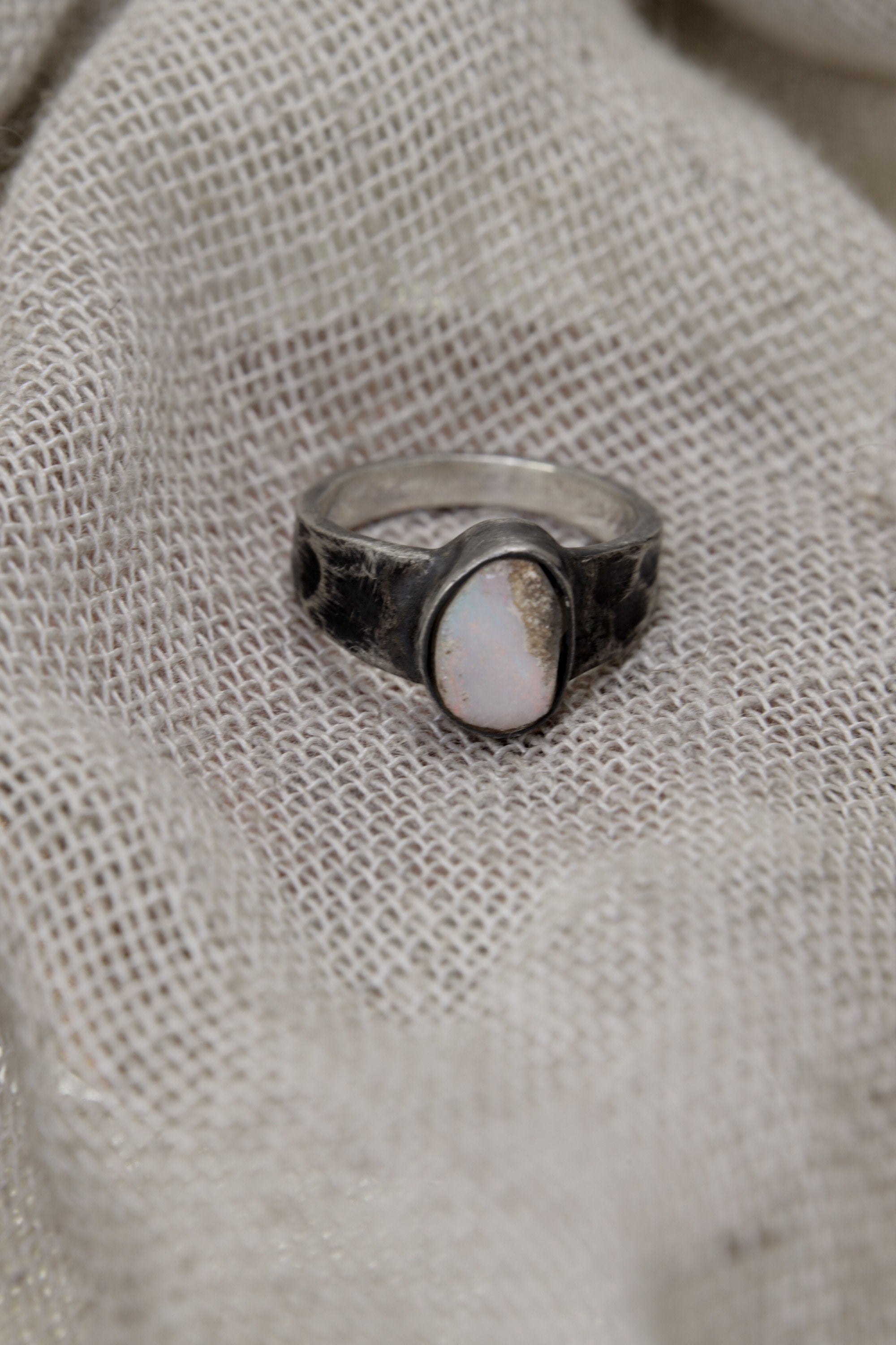 Lightning Ridge Gem Opal ring displayed on fabric, with lightly oxidized sterling silver setting and soft opal colour play.
