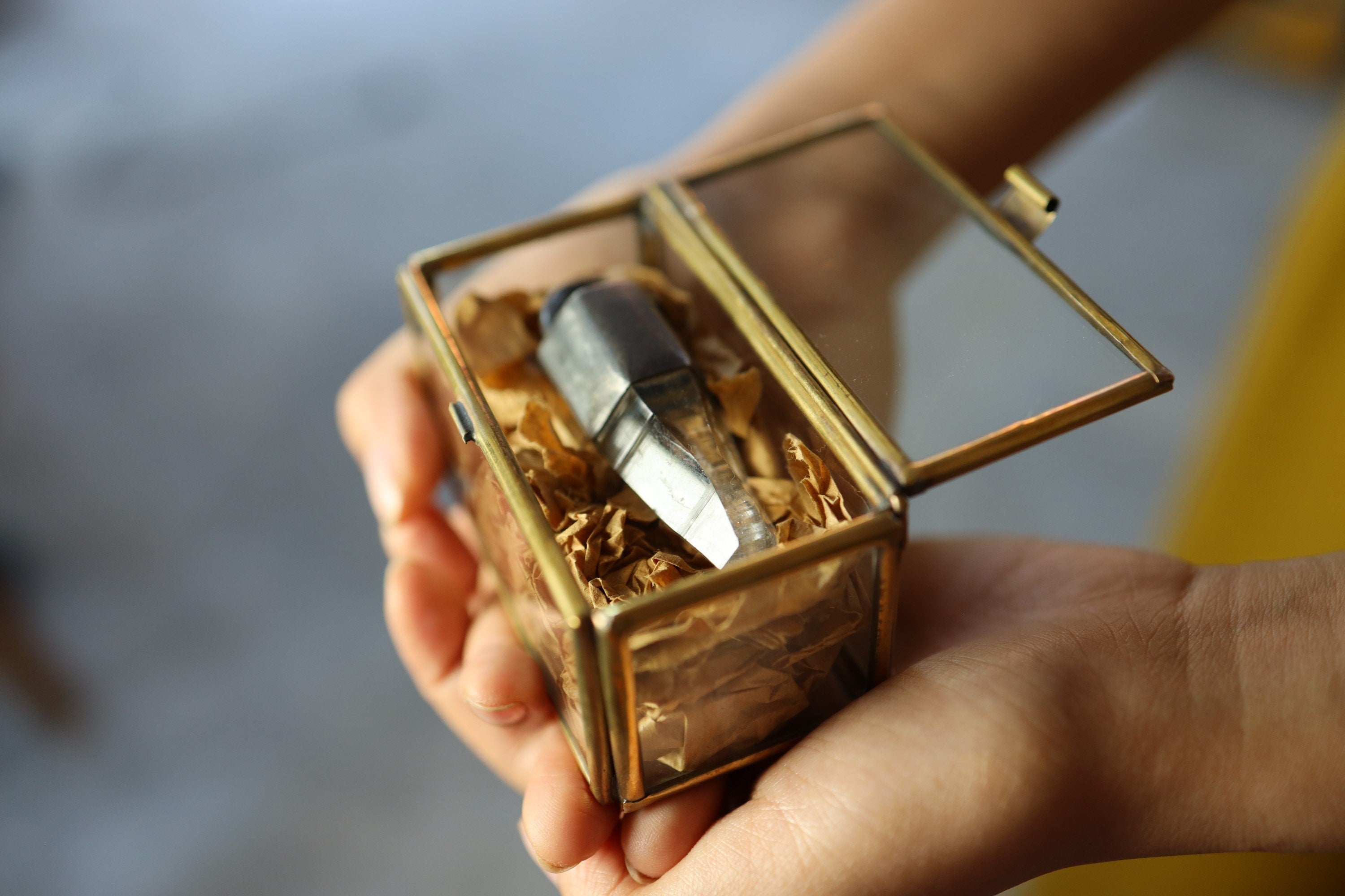 Rectangular premium gem display box held in hands, showing transparent glass and warm brass construction.
