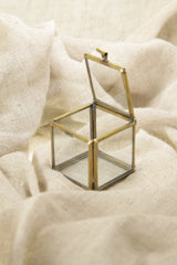 Gold-toned brass glass display box shown on soft fabric with open lid and clear square structure.