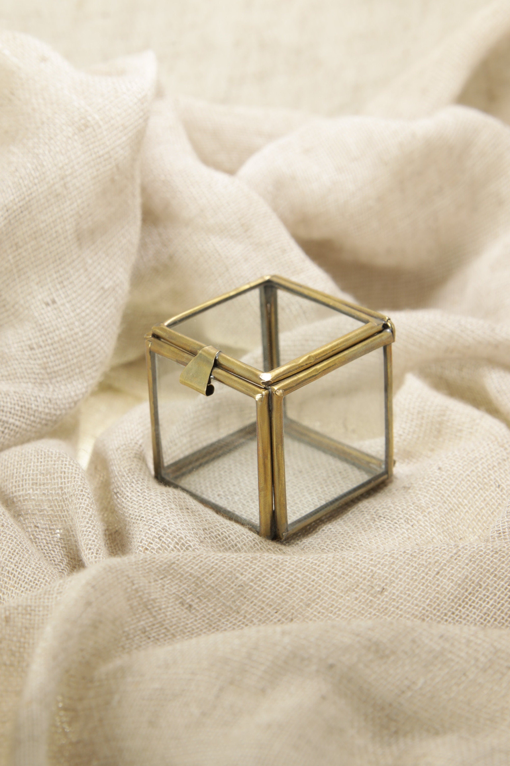 Brass and glass square display box styled on cream fabric, suitable for rings, earrings, and tiny keepsakes.