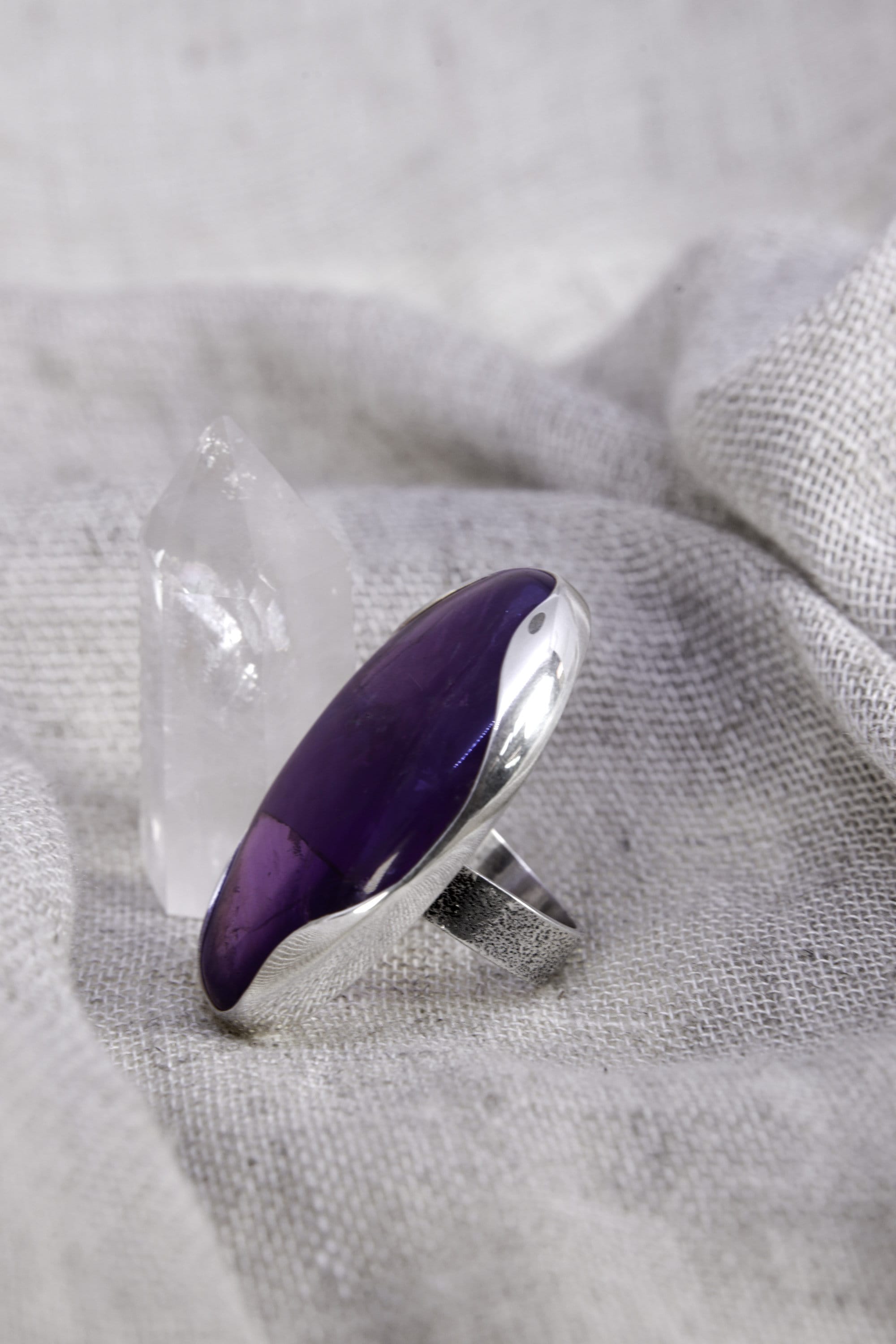Side view of oval Amethyst ring showing polished purple quartz, high-shine sterling silver, and raised waved bezel setting.