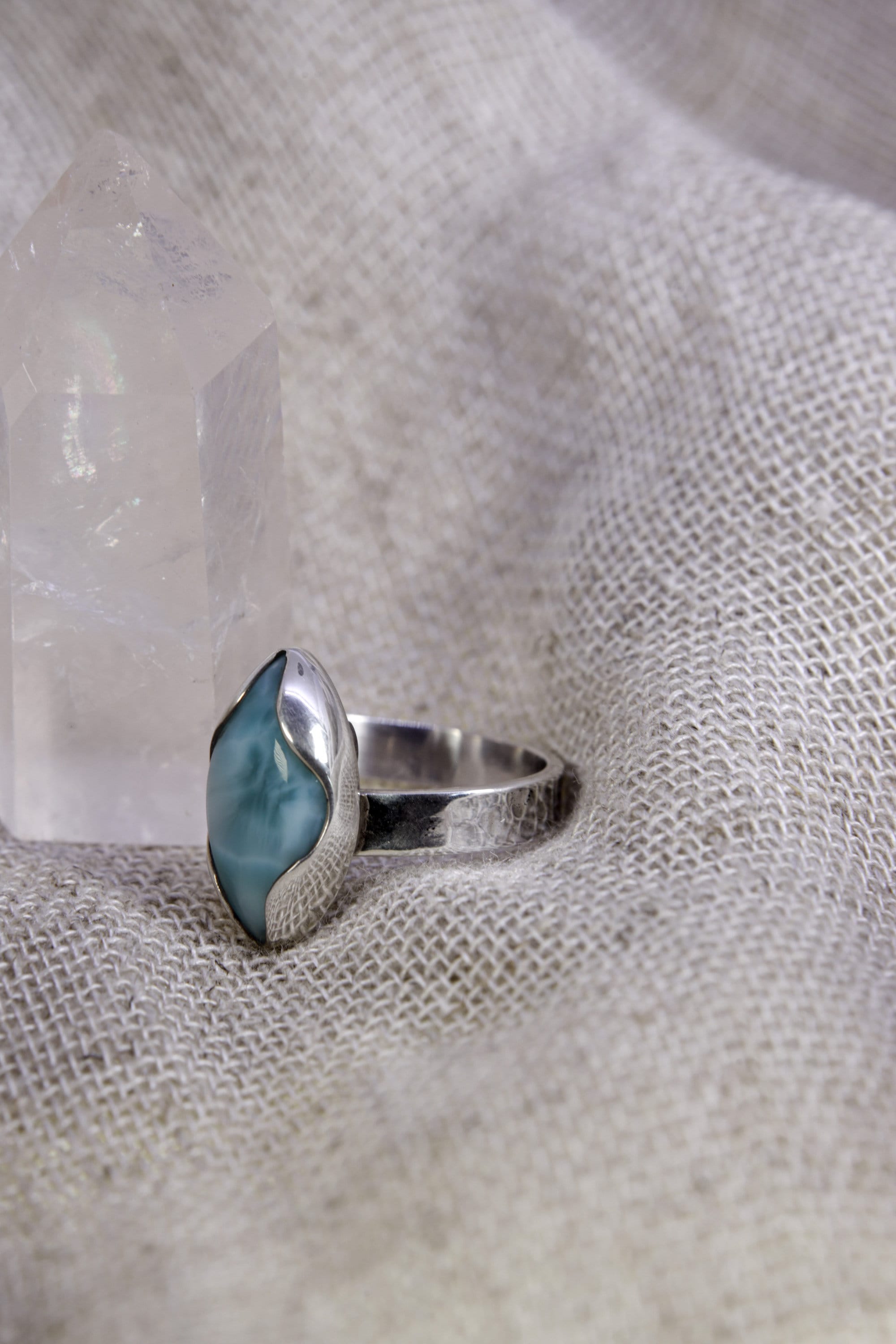 Eye of the Sea Larimar ring shown on soft fabric, with adjustable 925 sterling silver band and blue wave-like stone pattern.