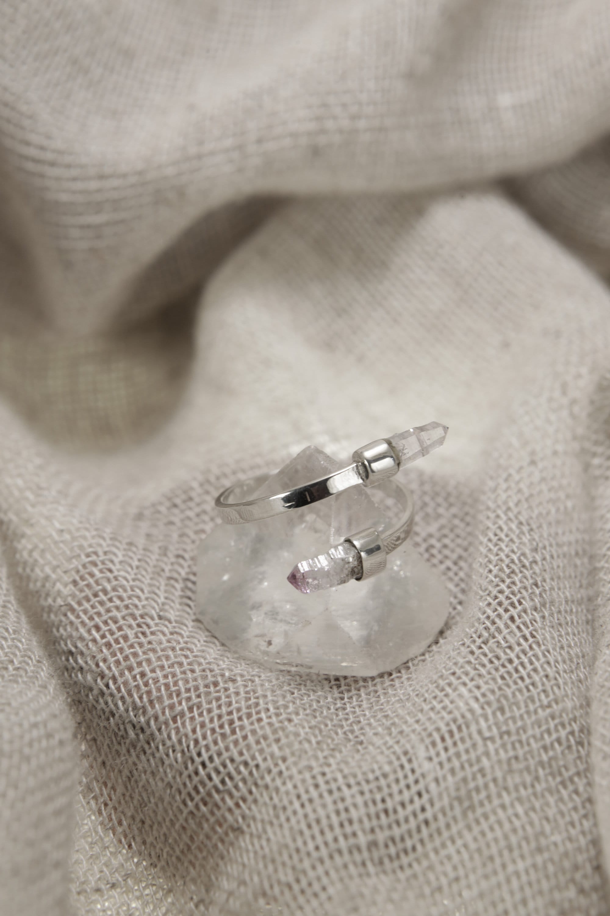 Amethyst Embrace Ring shown on soft fabric with adjustable sterling silver band and two pale purple Amethyst stones.