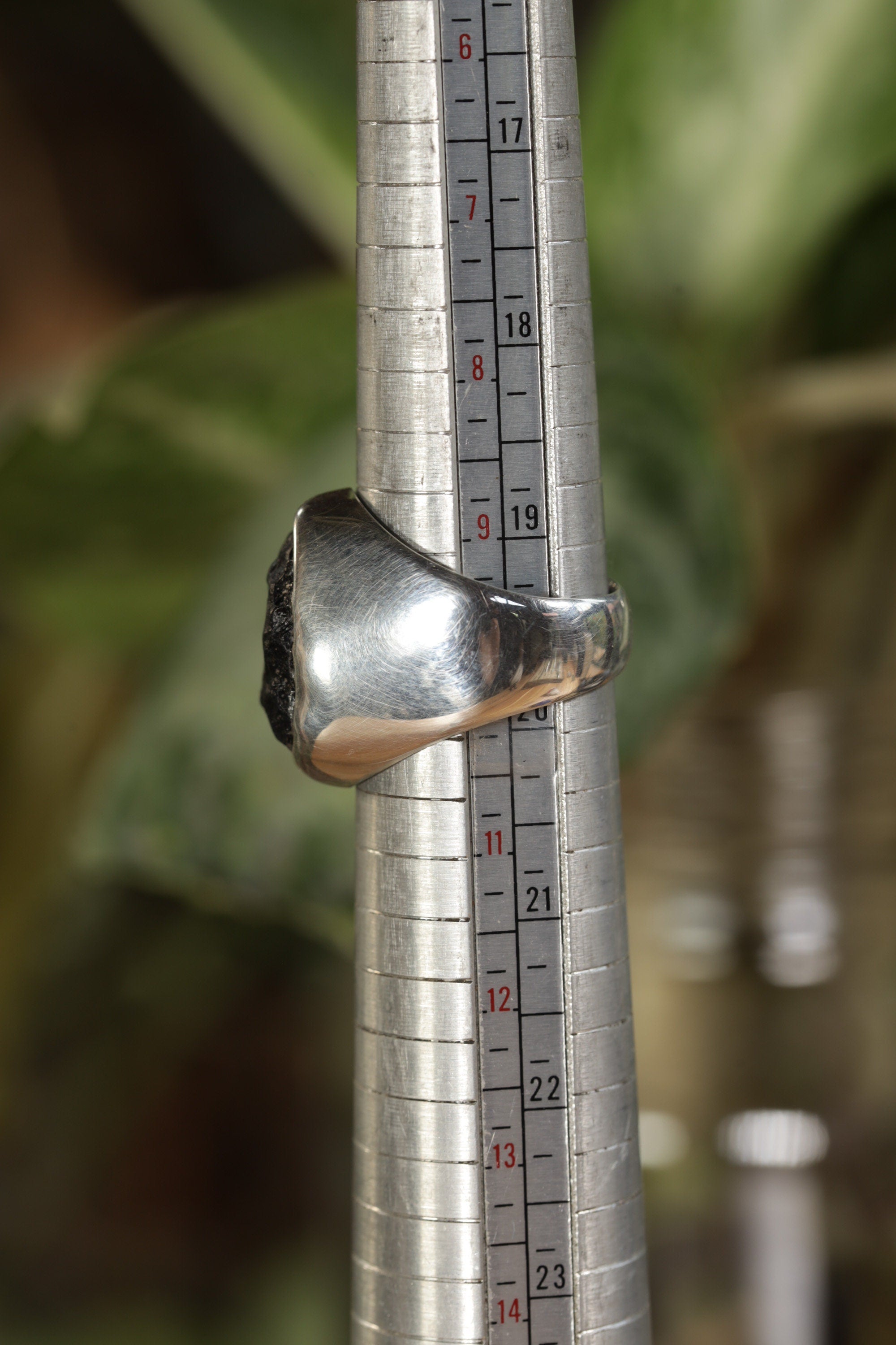 A silver ring with a black stone set in a bezel setting. The ring is sized on a ring sizer, showing a size 10.