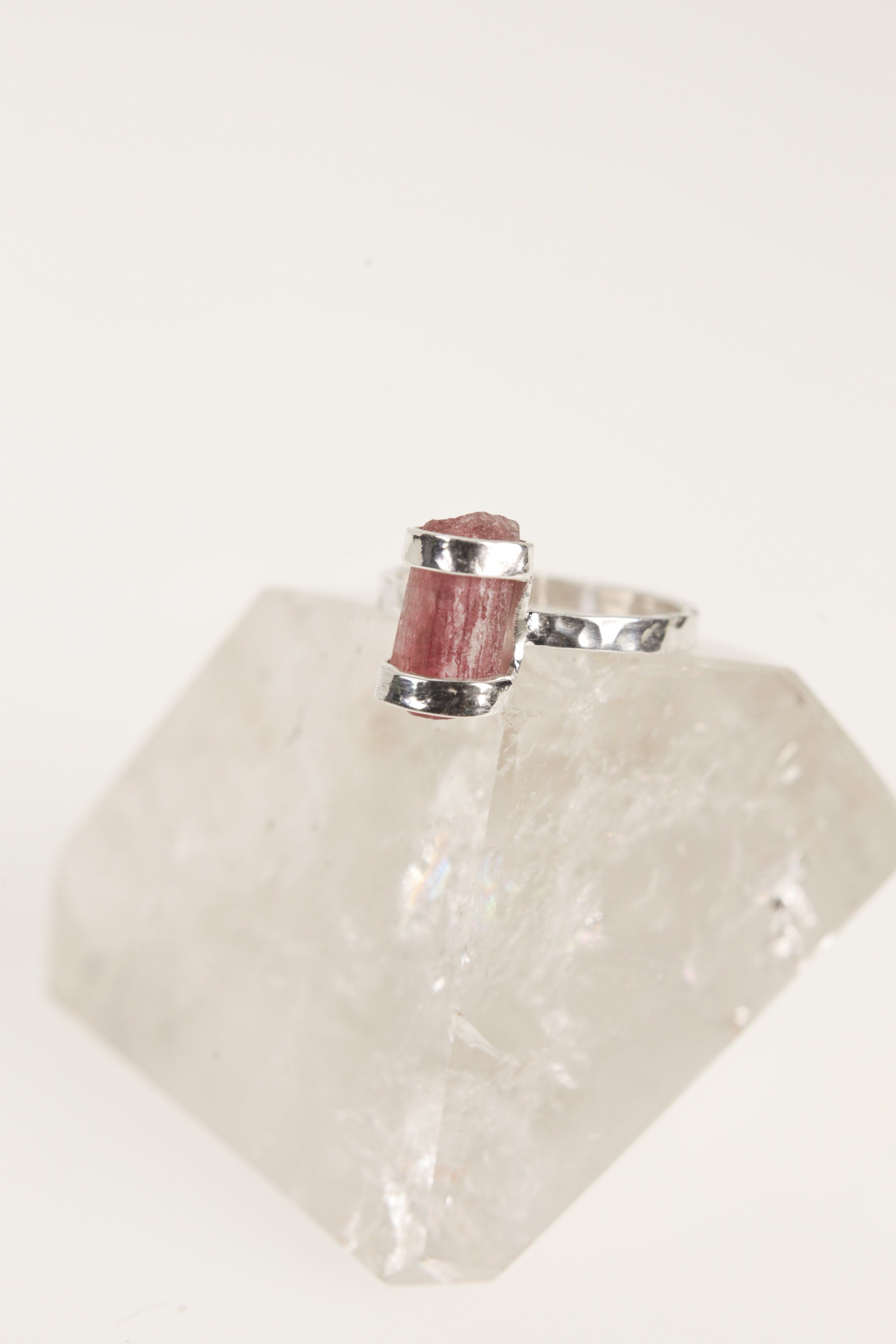 Raw Pink Tourmaline sterling silver ring displayed on clear quartz, with hammered silver band and natural rose crystal texture.