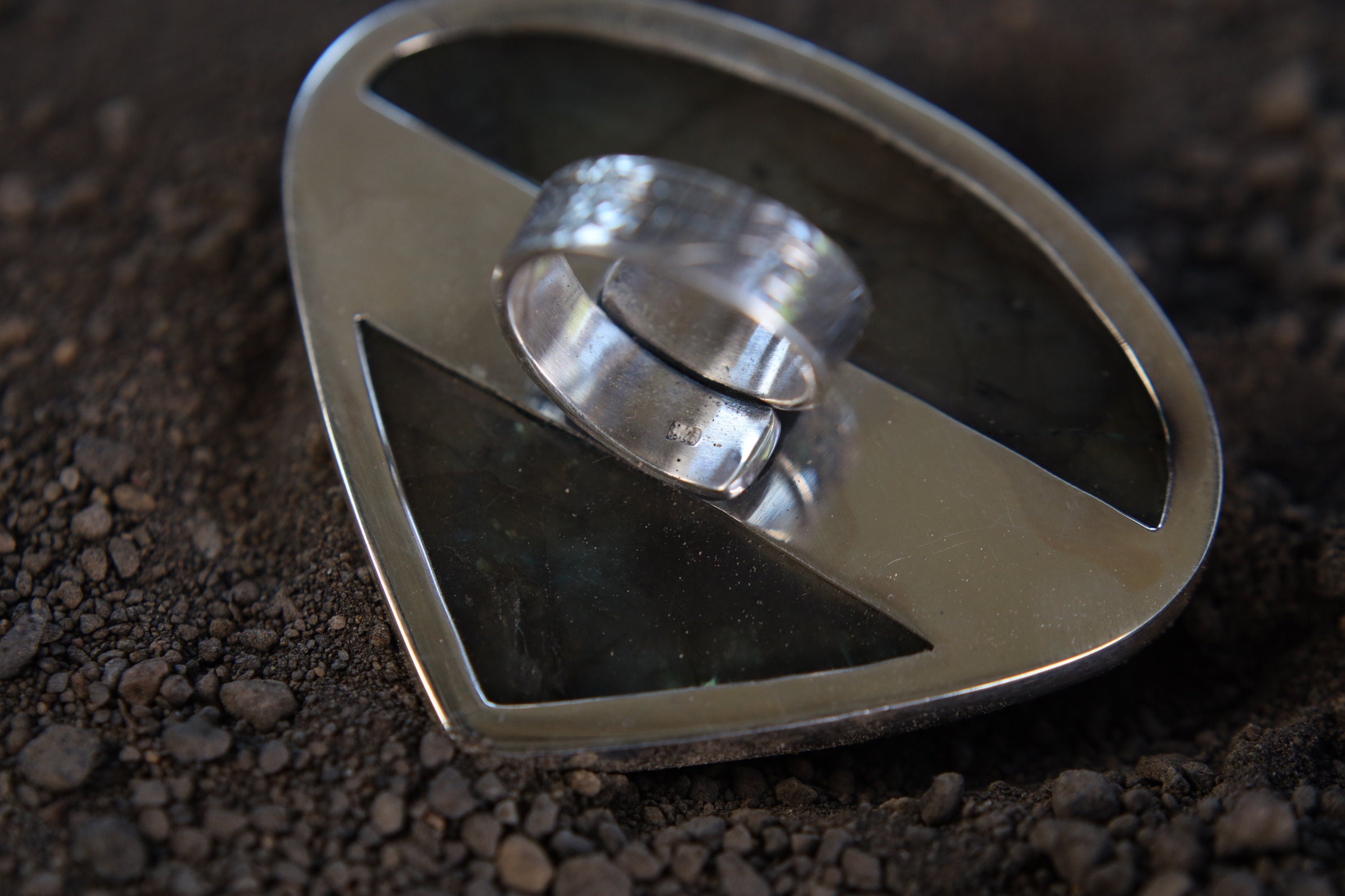 Teardrop Labradorite ring shown on earthy background, with waved bezel setting and shifting aurora-like colour flash.