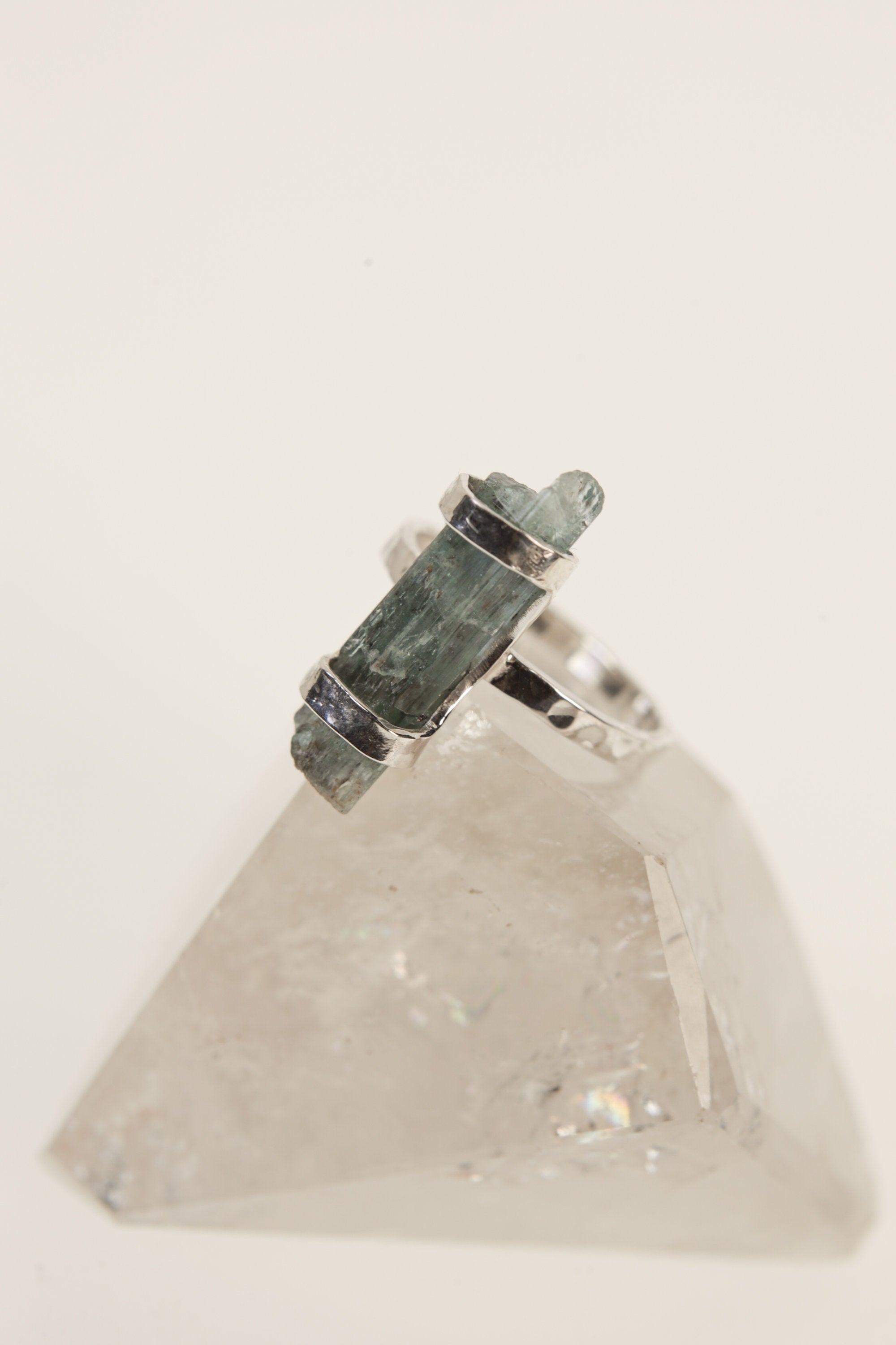 Himalayan Aquamarine ring displayed on clear quartz, with oxidized sterling silver setting and blue-green gemstone.