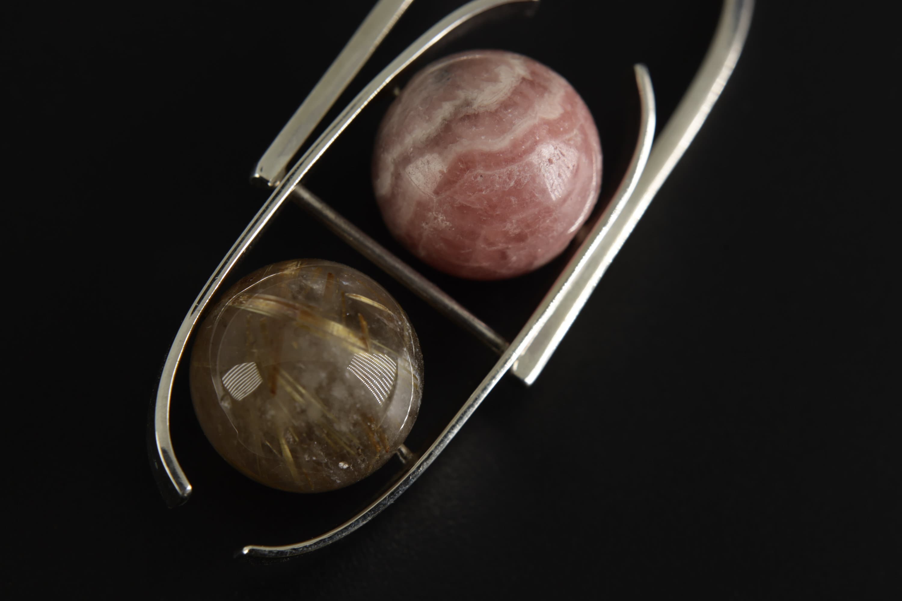 Macro detail of wheel-shaped Rhodochrosite and Golden Rutile Quartz in a bright 925 sterling silver pendant setting.