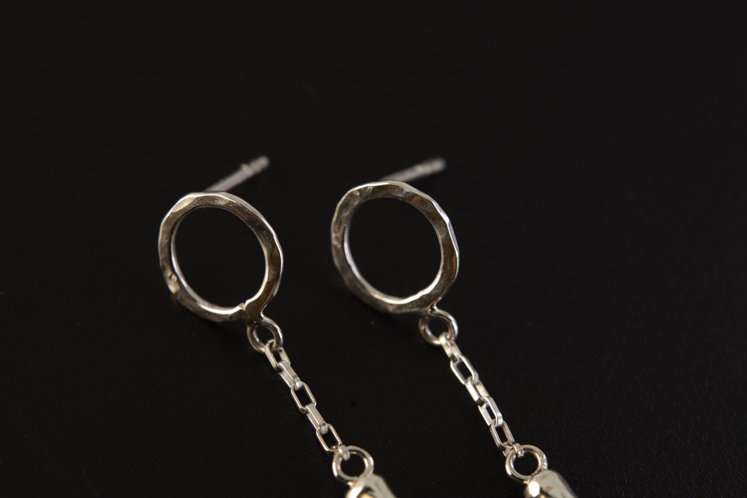 Close view of sterling silver Green Tourmaline earrings showing hammered round studs, chain dangles, and raw green crystals.