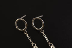Close view of sterling silver Green Tourmaline earrings showing hammered round studs, chain dangles, and raw green crystals.