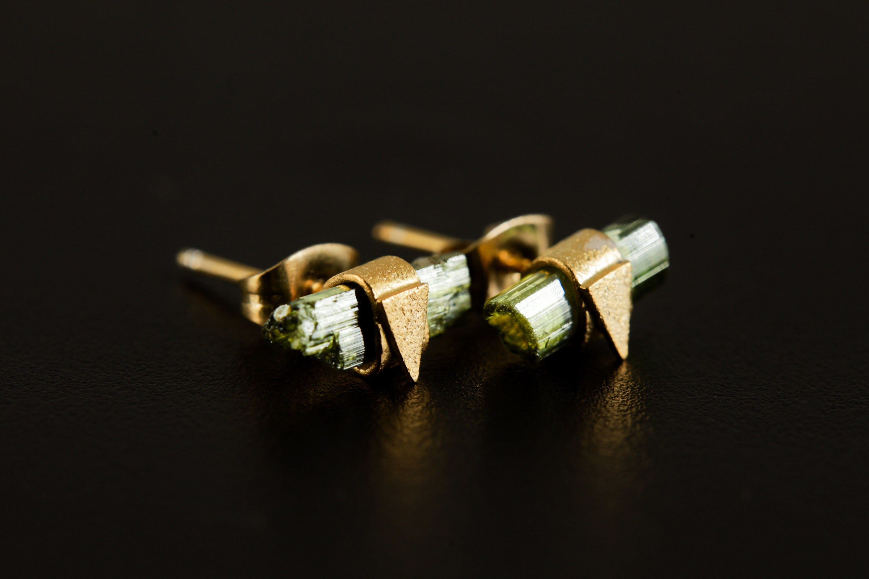 Handmade Green Tourmaline stud earrings displayed on dark background with raw stones and triangle settings.