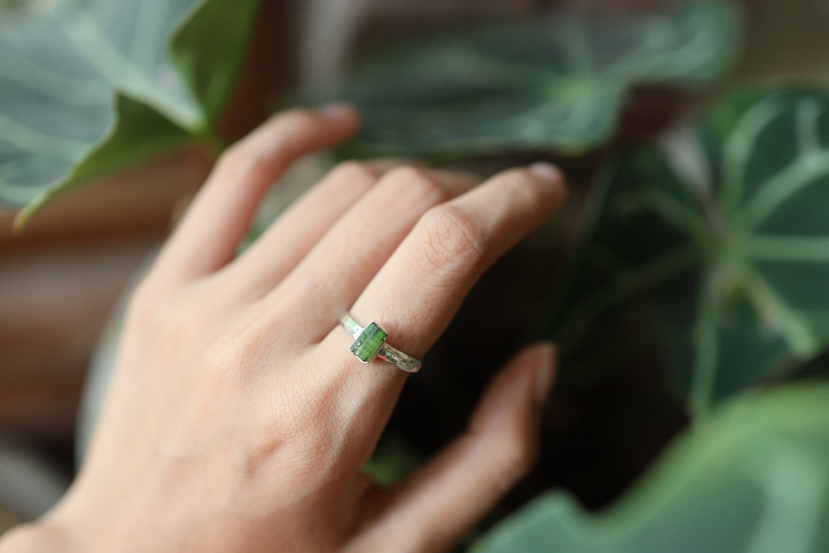 Green Tourmaline silver ring shown worn on a hand, with polished hammered sterling silver and forest-green gemstone.